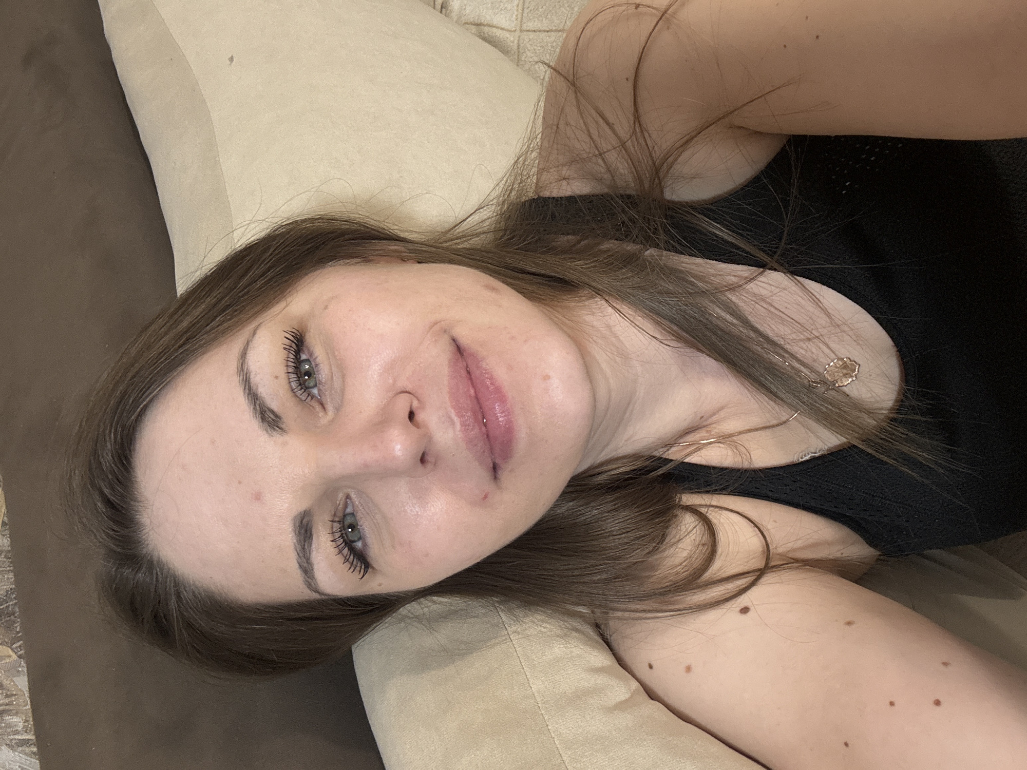 A woman with long brown hair is lying on a beige couch. She is wearing a black top. The setting appears to be indoors. There is no information to link this image to the city of Раздолье, Russia.