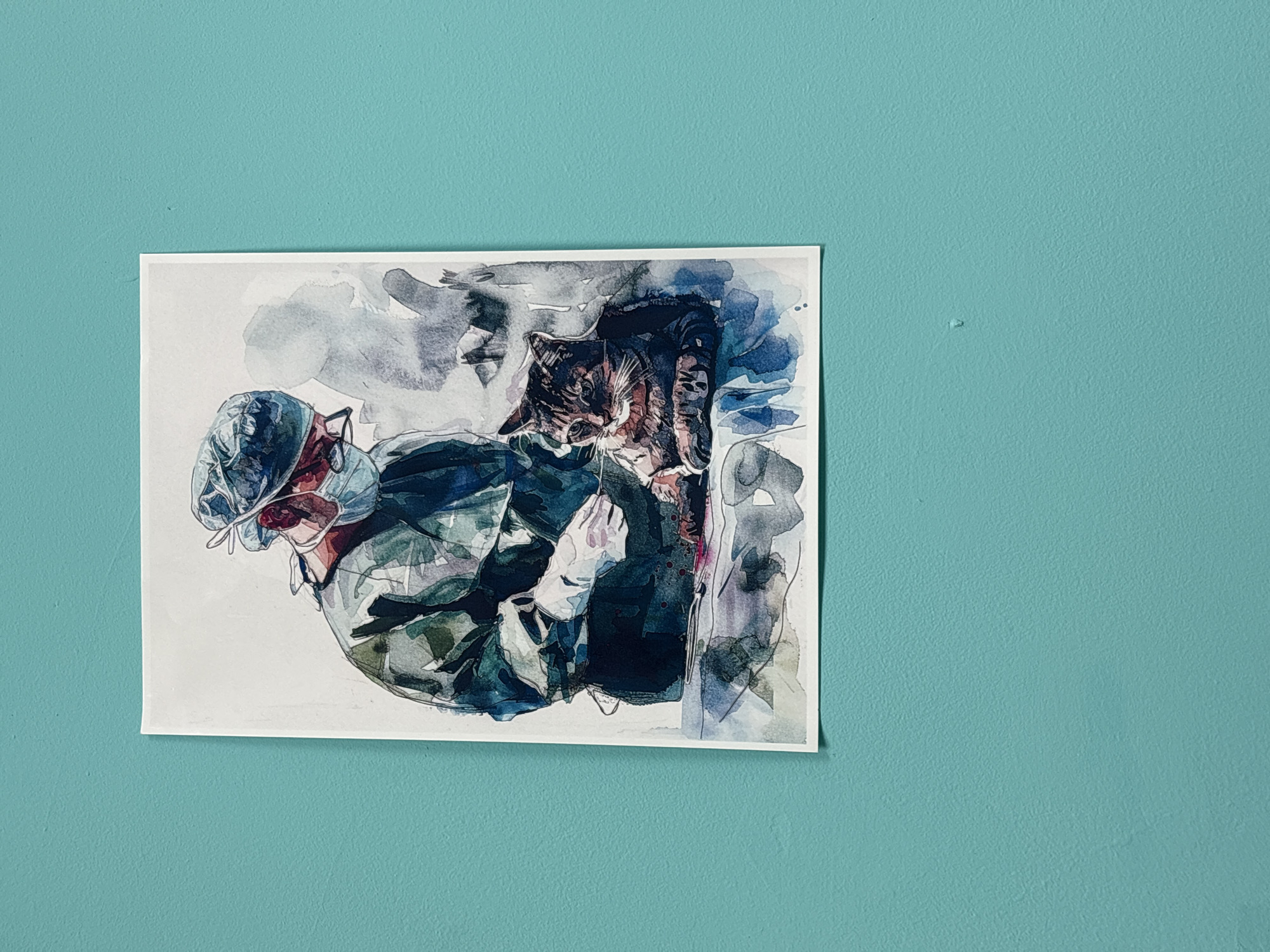A watercolor painting of a person wearing medical attire holding a cat is hung on a light blue wall. The painting is oriented at a slight angle. The wall appears to be lightly textured. The scene is in an indeterminate location, not clearly identifiable as Izhevsk, Russia.