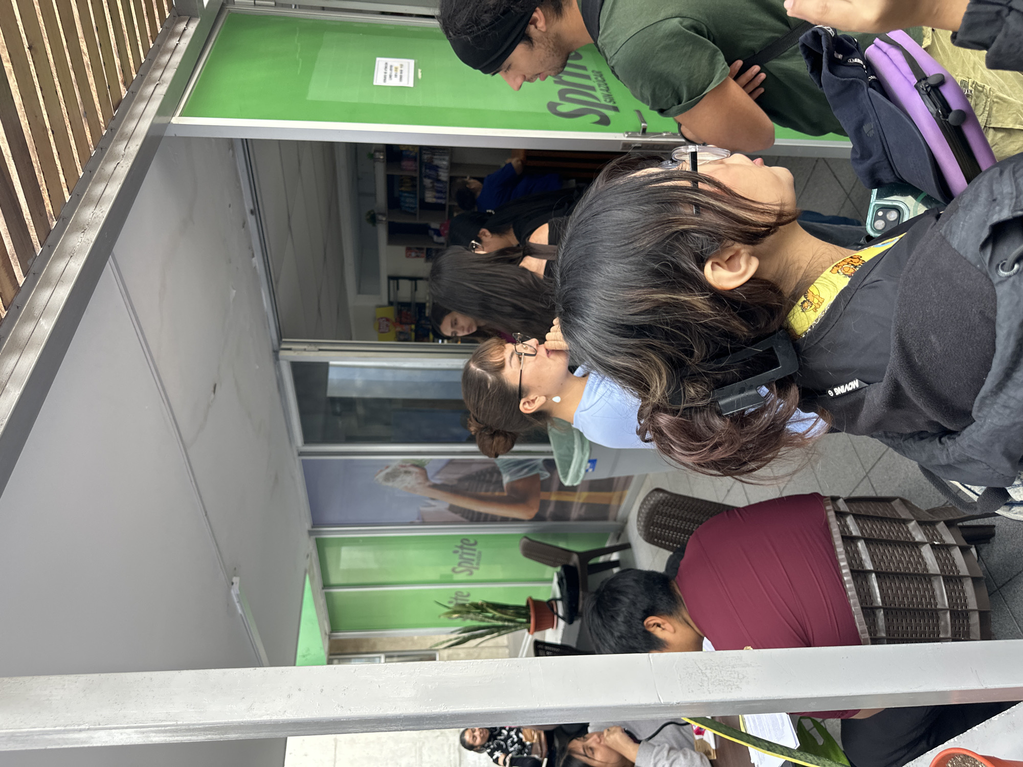 The image shows a line of people in front of a store in Arica, Chile. The store's windows have "Sprite" logos on them. People are standing outside the storefront. Some of the people are looking towards the store. The scene appears to be outside during the day.