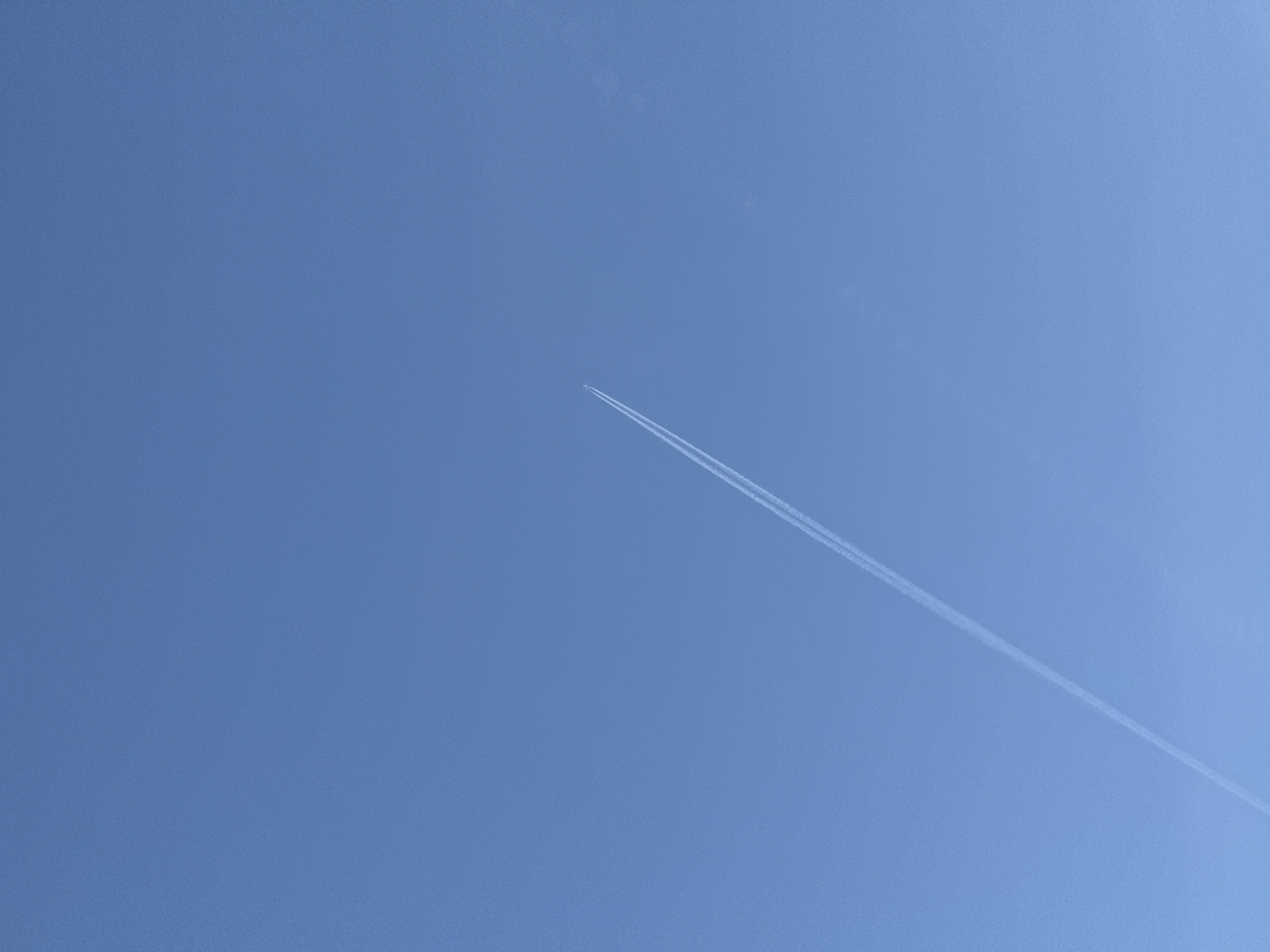 The image depicts a clear, blue sky. A single contrail is visible, extending diagonally from the upper-center towards the lower-right corner of the frame. There are no other discernible objects or features in the sky, besides the plane. There is no indication of the location being in Yekaterinburg, Russia, nor are there any people visible.
