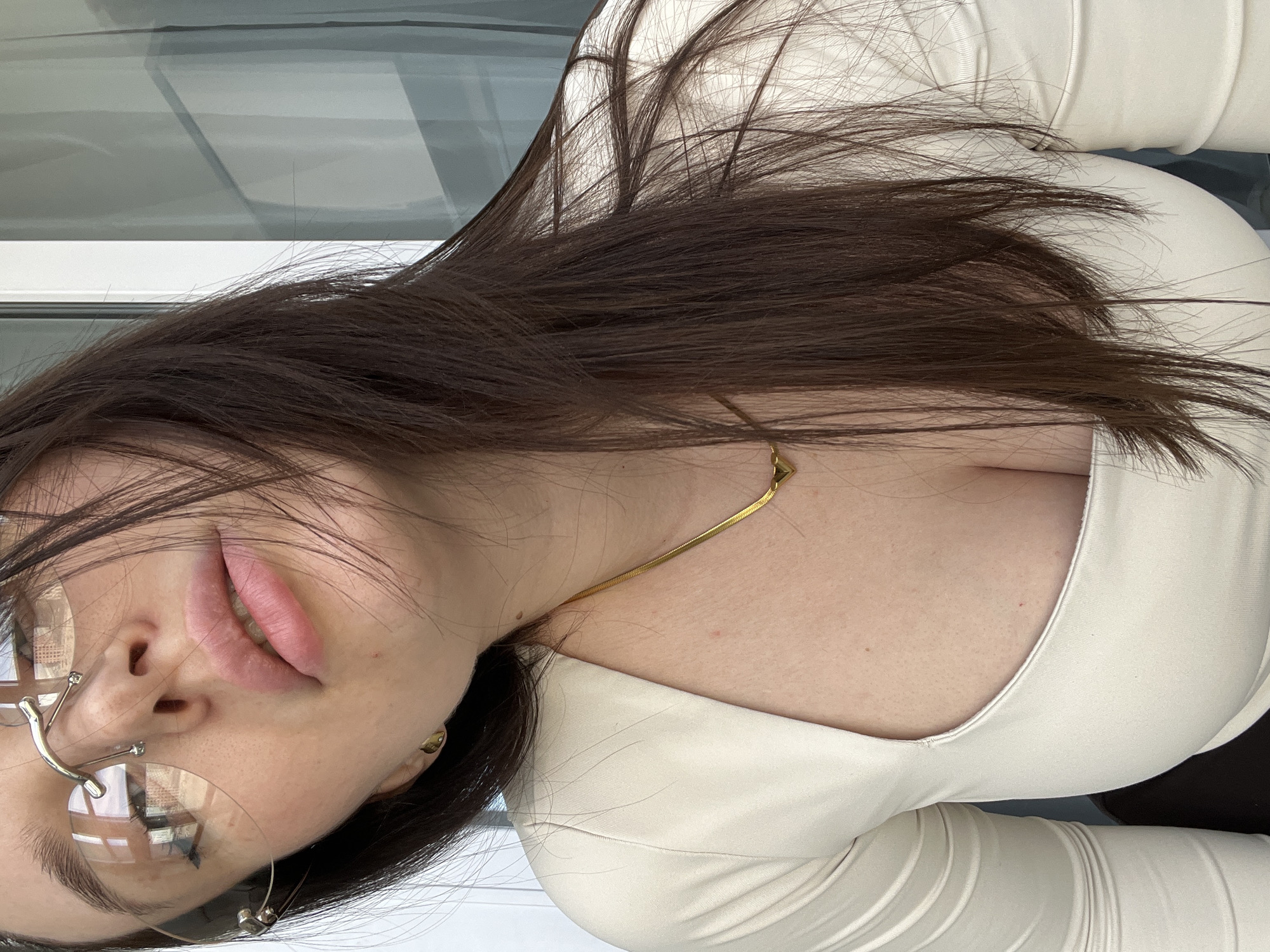 A woman is posing for a photograph. She has dark brown hair and is wearing glasses. She is wearing a light-colored top and a gold necklace. The location is not identifiable as being in Tyumen, Russia.