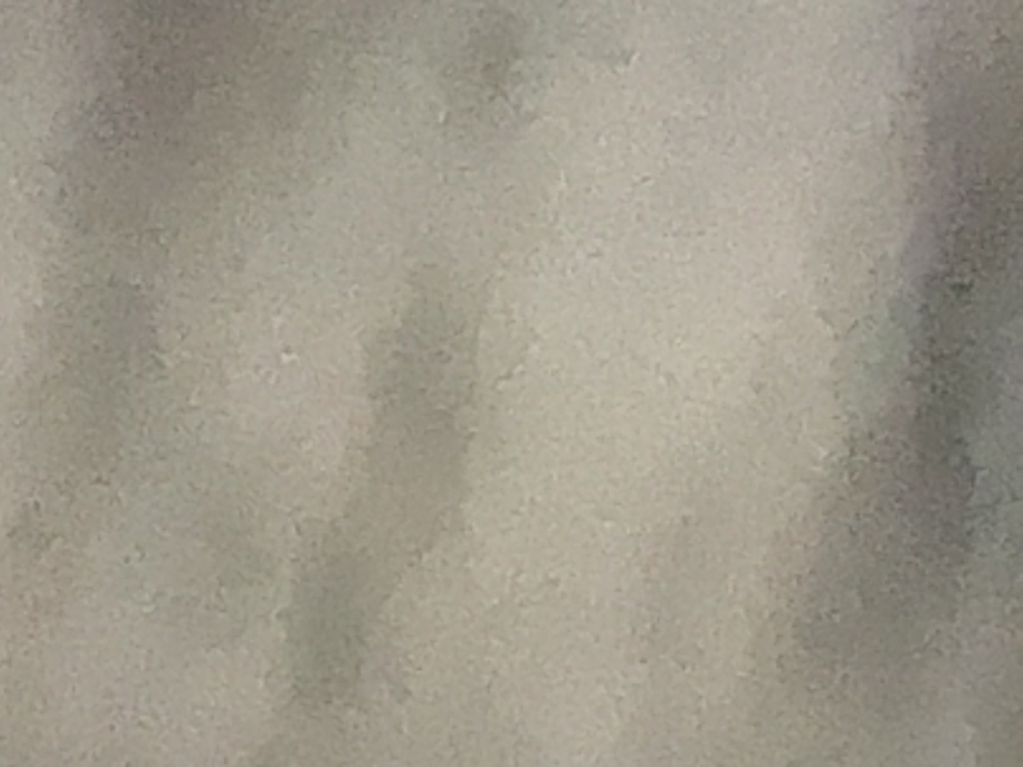 The image shows a blurry, textured surface with subtle variations in color, primarily shades of gray and beige. There are no discernible objects, people, or actions visible. The texture appears granular, similar to a rough wall or a fabric. The lighting is diffused, creating soft shadows and highlights across the surface. No specific location in Lokbatan, Azerbaijan can be identified from this image.