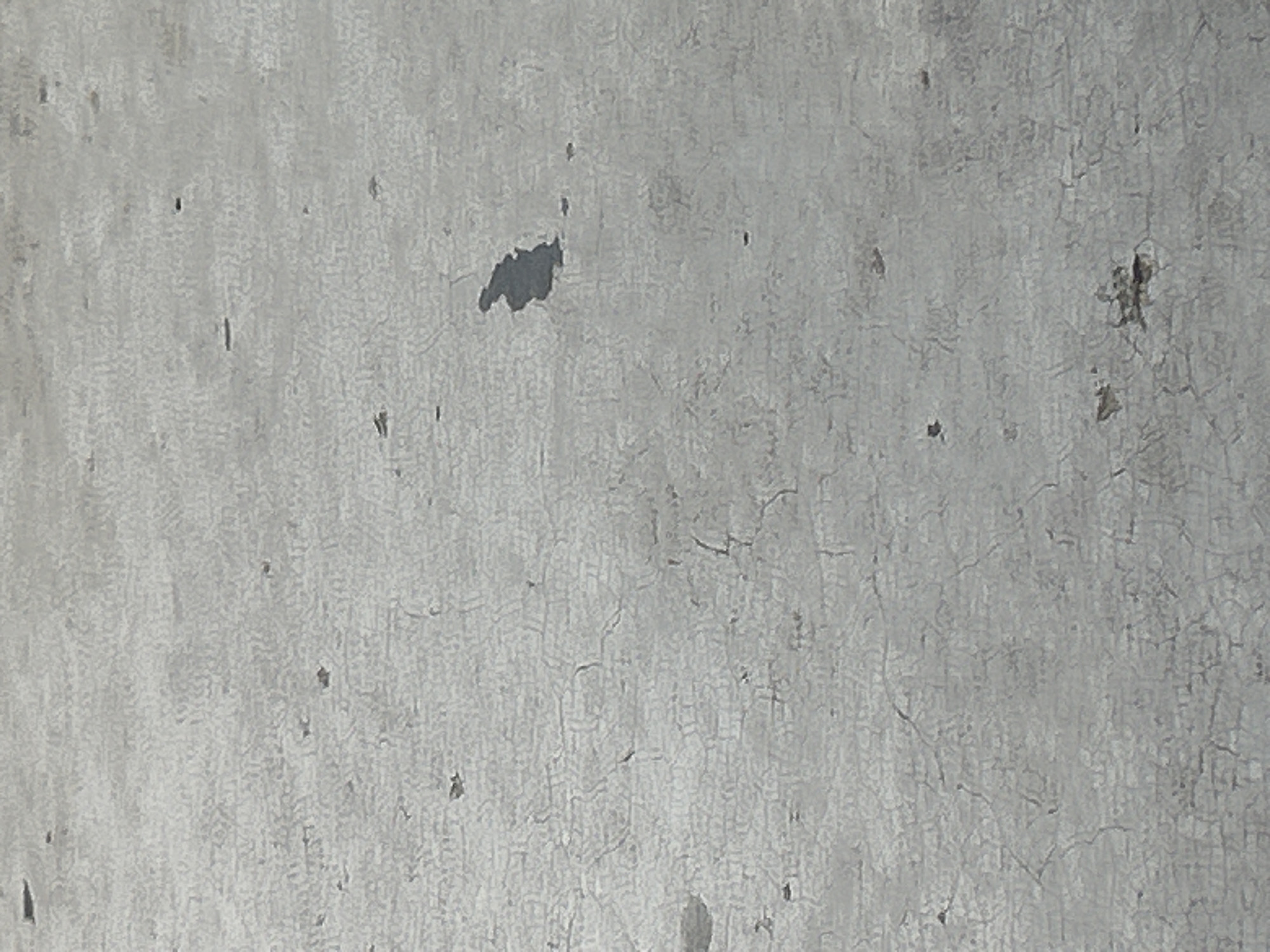 The image shows a close-up, overhead view of a cracked, grey, outdoor surface, possibly pavement or concrete. There are numerous small, dark specks scattered across the surface, and a larger, irregular dark patch in the upper right quadrant, which appears to be a puddle or a stain. The texture suggests an aged or weathered material. The location is identified as Santa Ana, Venezuela.