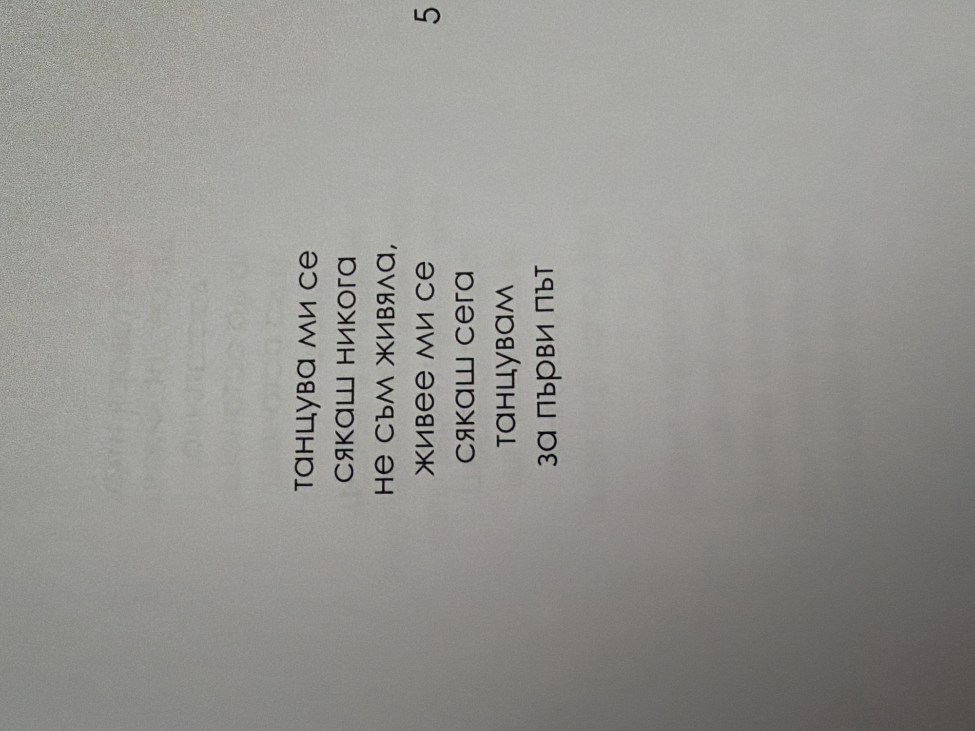 The image shows a page from a book or document with text in Bulgarian. The text is arranged in several lines, centered on the page. The lines read: "танцува ми се", "сякаш никога", "не съм живяла,", "живее ми се", "сякаш сега", "танцувам", "за първи път". There is also the number "5" to the right of the text, likely a page number. The background is a plain, light gray surface, possibly paper or a wall. There are no people, objects, or environmental details visible that would suggest a specific location in Pazardzhik, Bulgaria.