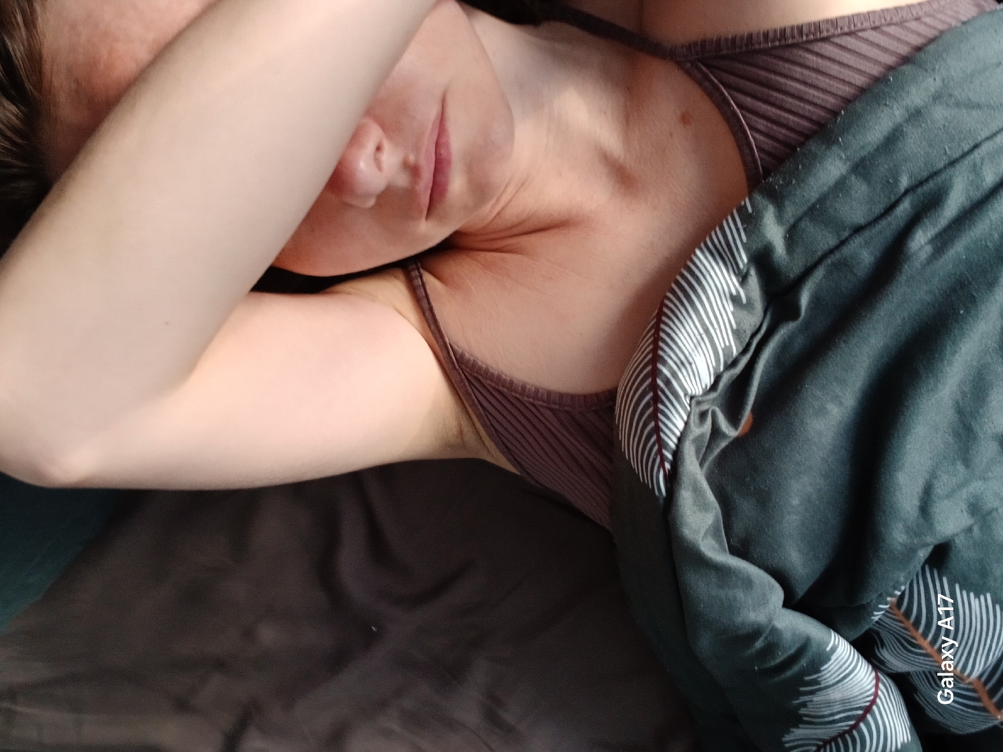 A woman is lying down, partially covered by a blanket. She is wearing a brown ribbed top. Her face is partially obscured by her arm. The blanket is dark gray with white and burgundy feather-like patterns. The image has a "Galaxy A17" watermark. The location in Yekaterinburg, Russia, cannot be determined from this image.