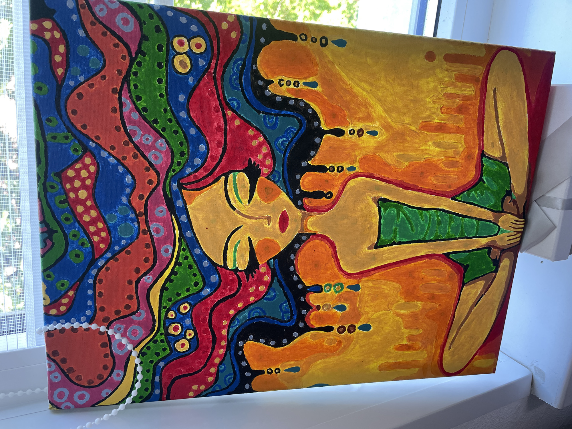 A vibrant, stylized painting on canvas is positioned horizontally on a white windowsill. The artwork depicts a figure, likely a woman, with golden-yellow skin, closed green eyes, and red lips. She is shown from the waist up, wearing a green garment, with her hands clasped together in front of her.
The most striking feature of the painting is the figure's hair, which is rendered as a cascade of broad, wavy, multi-colored ribbons in bright hues of red, blue, green, orange, pink, and yellow. These hair sections are adorned with various patterns, including polka dots and concentric circles, outlined boldly in black. The background behind the figure's body transitions from a bright yellow to an orange hue.
The painting's style is decorative and folk art-inspired, characterized by its bold outlines, saturated colors, and intricate patterns. Behind the canvas, a window with a white mesh screen is visible, through which green foliage from outside can be seen, suggesting an outdoor garden or trees. A white beaded chain is draped across the lower left corner of the canvas. There is no visible text in the image. The scene appears to be set indoors during daytime.