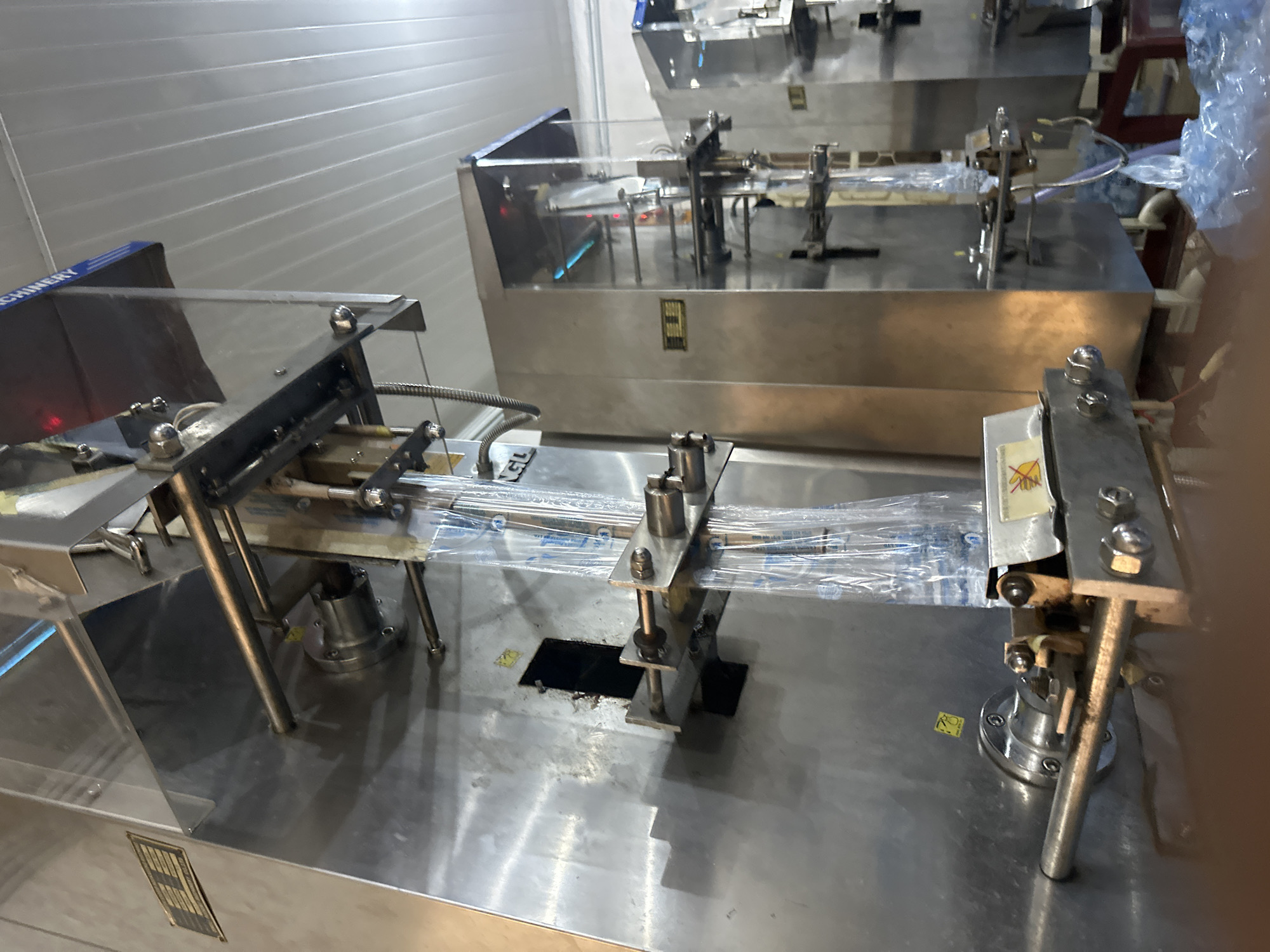 The image depicts a close-up view of a section of industrial packaging machinery. The equipment is made of stainless steel. The machine processes plastic-wrapped items. The setting appears to be a factory or manufacturing facility. No people are visible. There is no evidence to suggest the location of Jos, Nigeria.