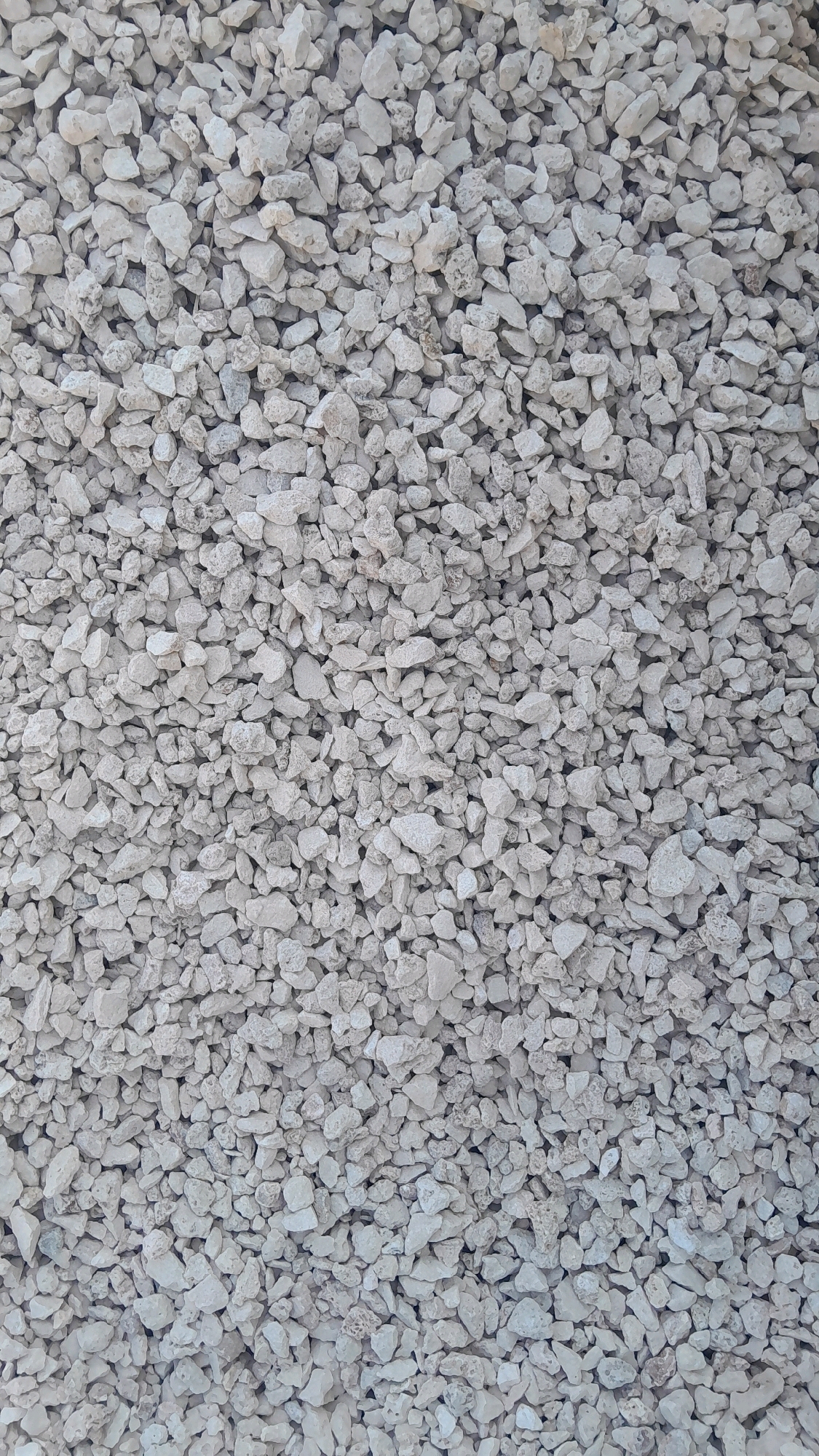 The image shows a close-up, overhead view of a large pile of light-colored, rough gravel. The gravel pieces are irregular in shape and size, with many sharp edges and porous surfaces. The overall texture is rough and granular. The lighting suggests an outdoor environment, with no discernible shadows to indicate a specific time of day. The background is entirely filled with the gravel, indicating a dense accumulation. There are no people, animals, or man-made structures visible in the frame. The location is described as Kedungtuban, Indonesia, but this context is not visually evident from the image itself.