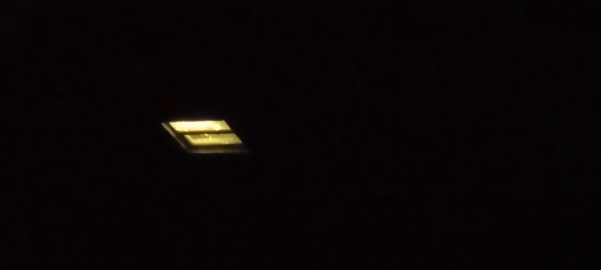 The image shows a dimly lit, dark background with a single, illuminated window. The window appears to be part of a building structure, with a warm yellow light emanating from within. The window itself seems to be divided into panes. The overall impression is of a solitary light in the darkness, possibly indicating nighttime or a poorly lit interior. There is no discernible location in the city of Kryvyi Rih, Ukraine, or any specific details about people, actions, or interactions.