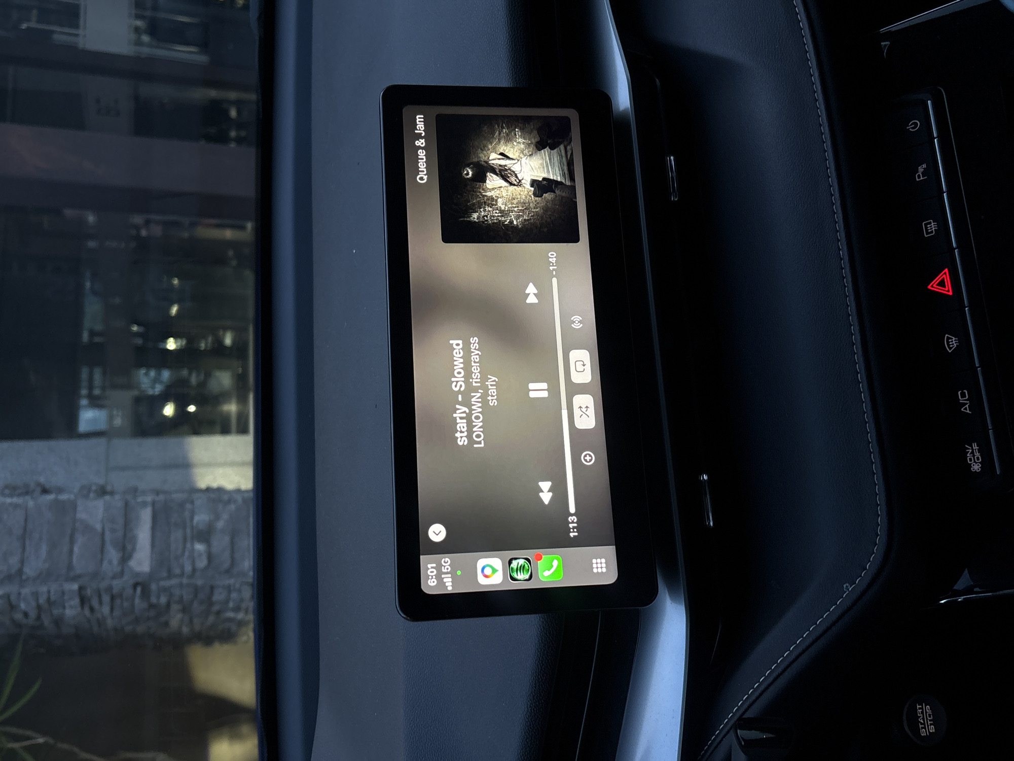 The image depicts the interior of a car, specifically the dashboard area, with a focus on the infotainment screen displaying a music player interface. The song "starly - Slowed" by LONOWN and riserayss is playing from the "Queue & Jam" playlist. The screen also shows standard mobile interface elements, such as cell service information, battery status, and various app icons. To the right of the screen are several buttons related to car functions, including hazard lights, parking assistance, and air conditioning.
Based on the presence of a car, dashboard, and surrounding elements, it's clear the scene is inside a vehicle. The image does not provide any information about the city of San Bernardino Tlaxcalancingo, Mexico. There are no people visible in the photograph.