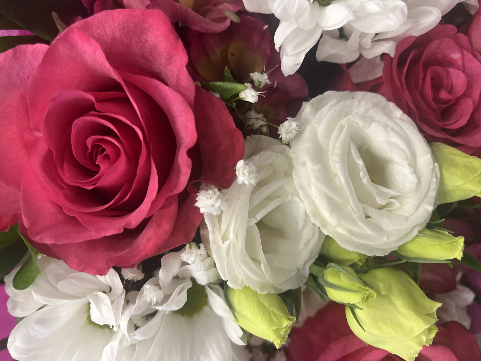 The image depicts a close-up of a bouquet of flowers. There are pink roses, white roses, and white chrysanthemums. The roses are fully open, while some of the chrysanthemums are still closed. Small white flowers, possibly baby's breath, are also visible. The flowers are tightly packed together, creating a dense arrangement. The image does not depict any location.