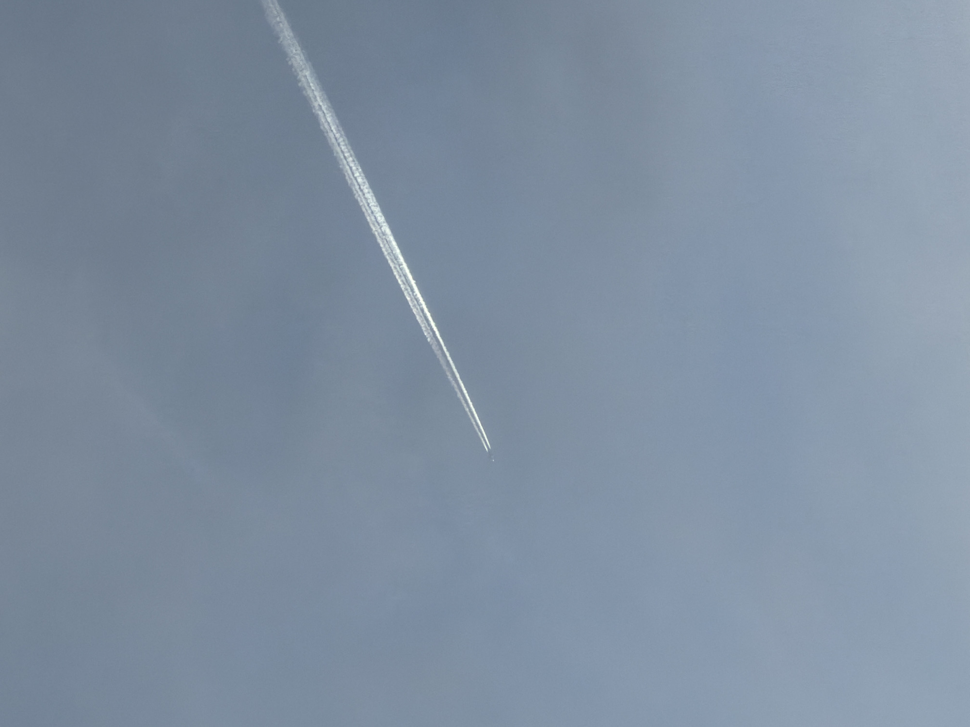 The image shows a plane with a contrail in a light blue sky. There is no indication the image was taken in Chaikovsky, Russia.
