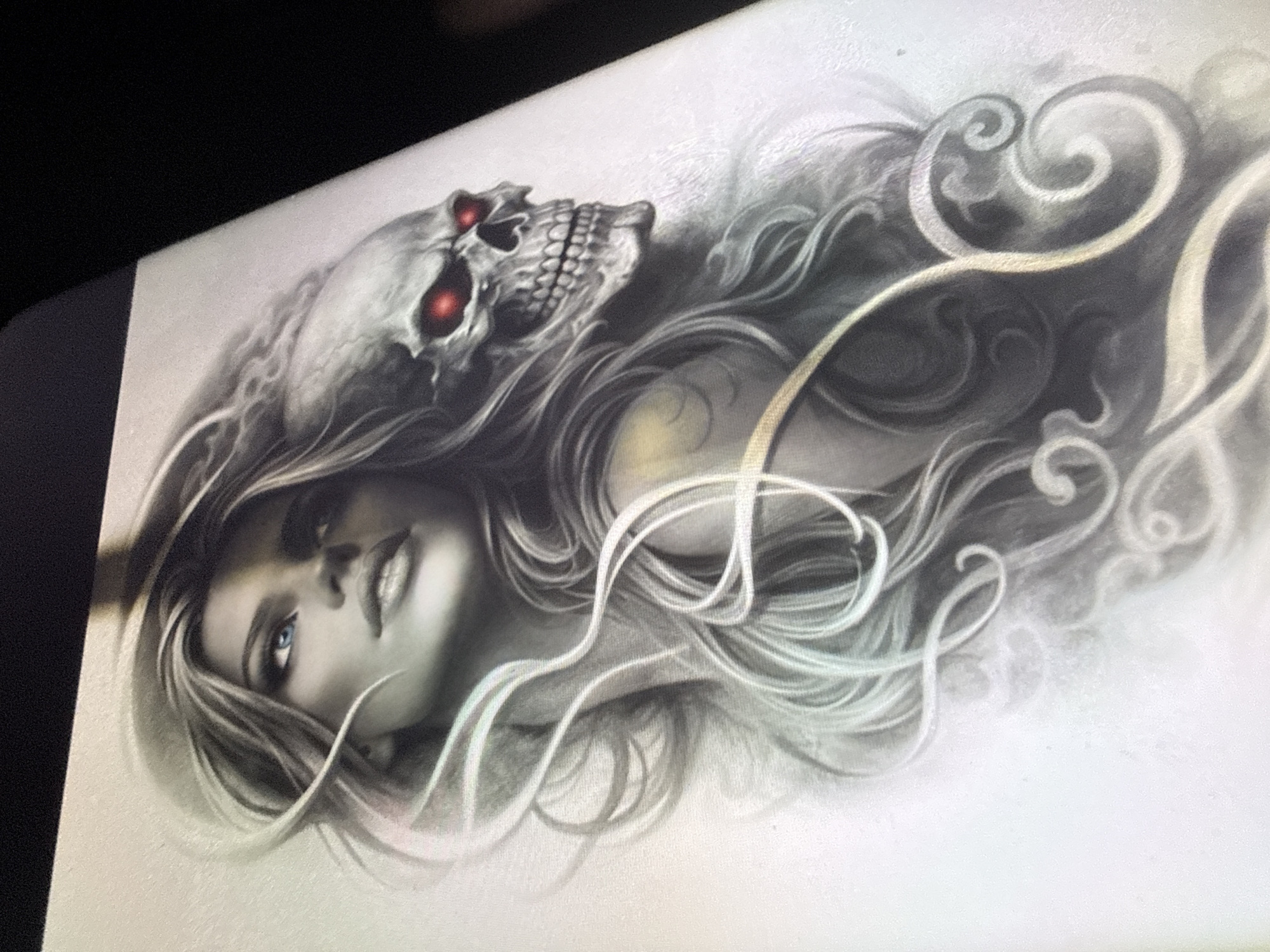 The image displays a digitally rendered artwork of a woman and a skull. The woman has long, flowing hair and is looking upwards with striking blue eyes. Her expression is serene. Juxtaposed behind her, and partially emerging from her hair, is a detailed skull with glowing red eyes. The artwork has a monochromatic aesthetic with subtle shading and highlights, creating a dramatic and somewhat eerie effect. The background is plain and light-colored. There is no identifiable location in the city of Sofia, Bulgaria, depicted in this image.