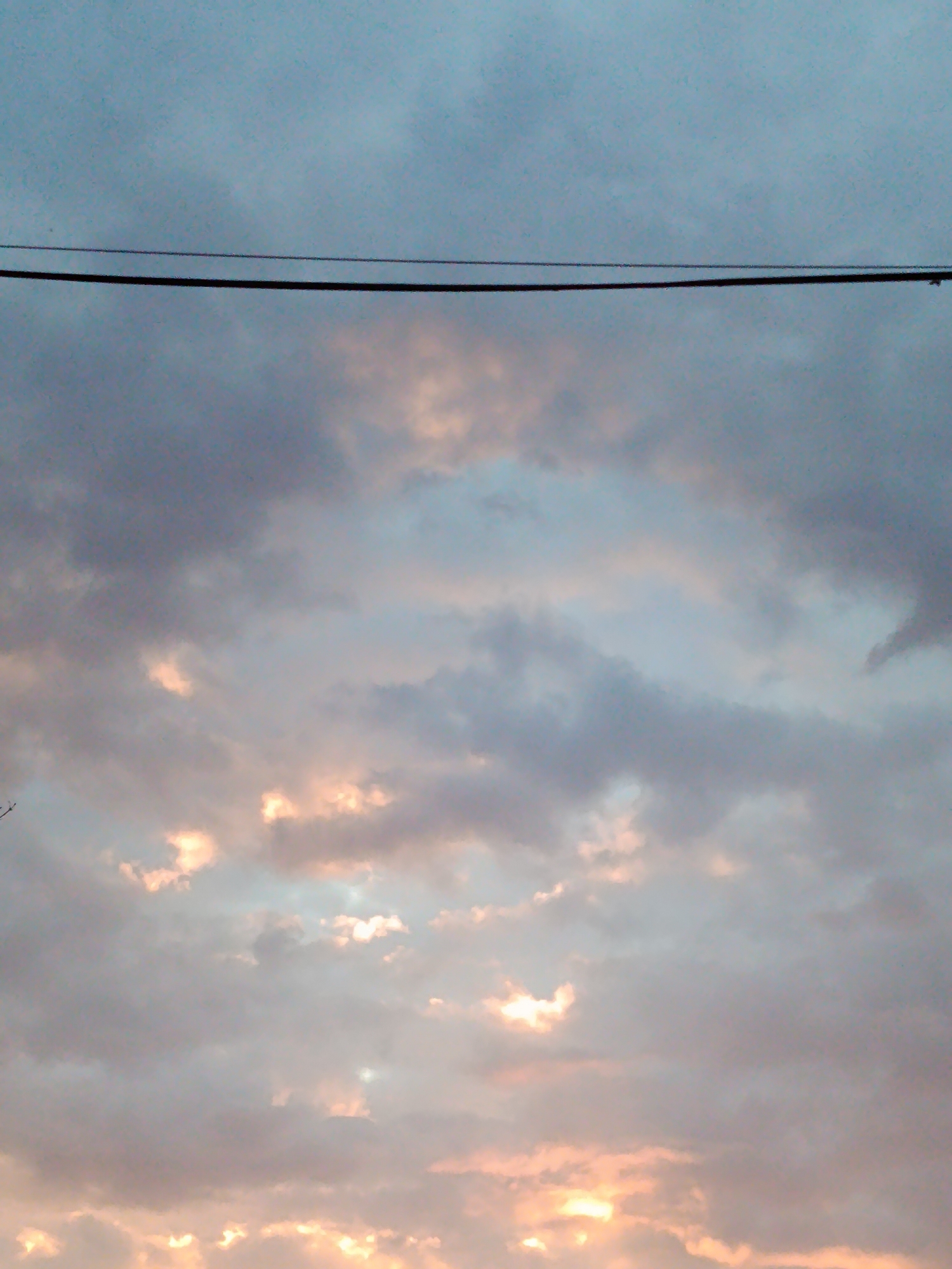 This image shows a cloudy sky with hints of pink and orange hues, suggesting it may be dawn or dusk. A dark, thin wire stretches horizontally across the upper portion of the frame. No people or specific landmarks are visible. The scene is likely outdoors, in an open area, and does not provide any specific visual cues to pinpoint its location within the city of Marx, Russia.
