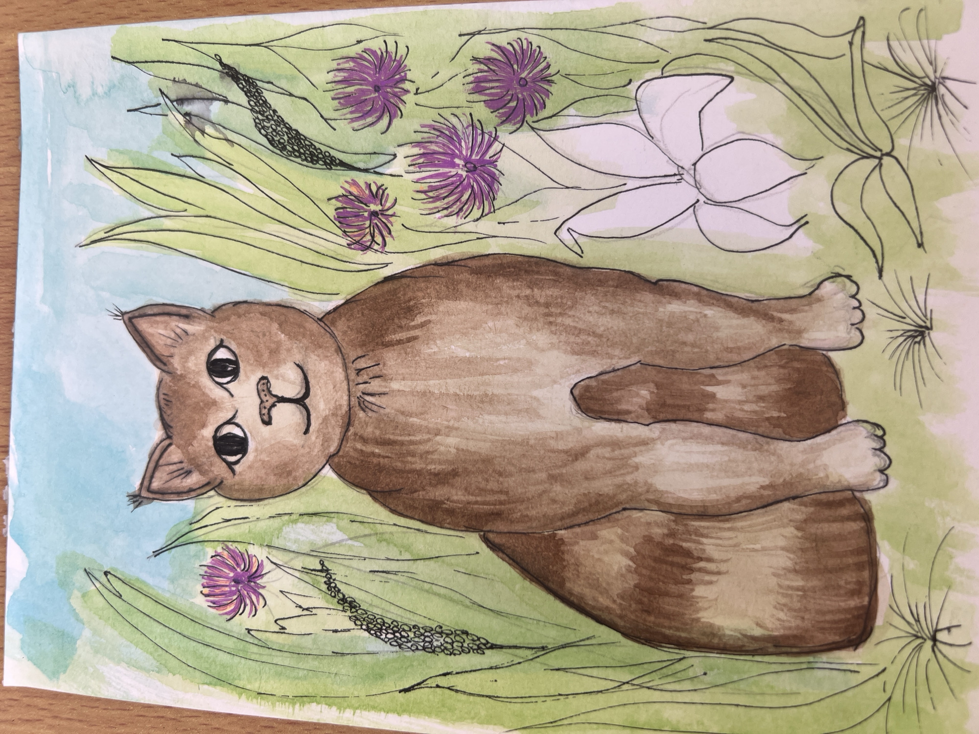 An illustration of a brown cat lying on its back in a field of flowers and grass is presented. The background is a light, washed-out green and blue watercolor, with darker green lines representing blades of grass. The flowers are a mix of purple thistle-like blooms and a single white lily in outline. The cat is rendered in shades of brown watercolor, with a simplistic, cartoonish face. The image is brightly lit and appears to be a scan or photograph of a handmade artwork on paper. The location is not evident.