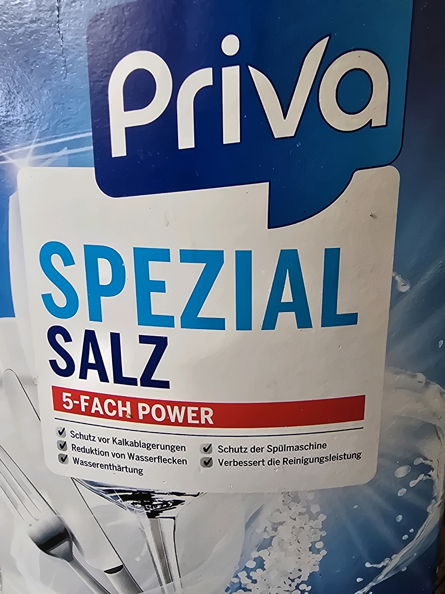The image displays a close-up of a product label for "Priva Spezial Salz" which appears to be dishwasher salt. The label features the brand name "Priva" in large white letters against a blue background, followed by "SPEZIAL SALZ" in large blue and dark blue letters respectively. Below this, a red banner reads "5-FACH POWER". A list of benefits is presented with checkmarks, including "Schutz vor Kalkablagerungen" (Protection against limescale deposits), "Reduktion von Wasserflecken" (Reduction of water spots), "Wasserenthärtung" (Water softening), "Schutz der Spülmaschine" (Protection of the dishwasher), and "Verbessert die Reinigungsleistung" (Improves cleaning performance). The background of the label shows imagery of clean dishes and water droplets. The overall scene is a product shot. There is no discernible information about the city of Hamminkeln, Germany in the image.