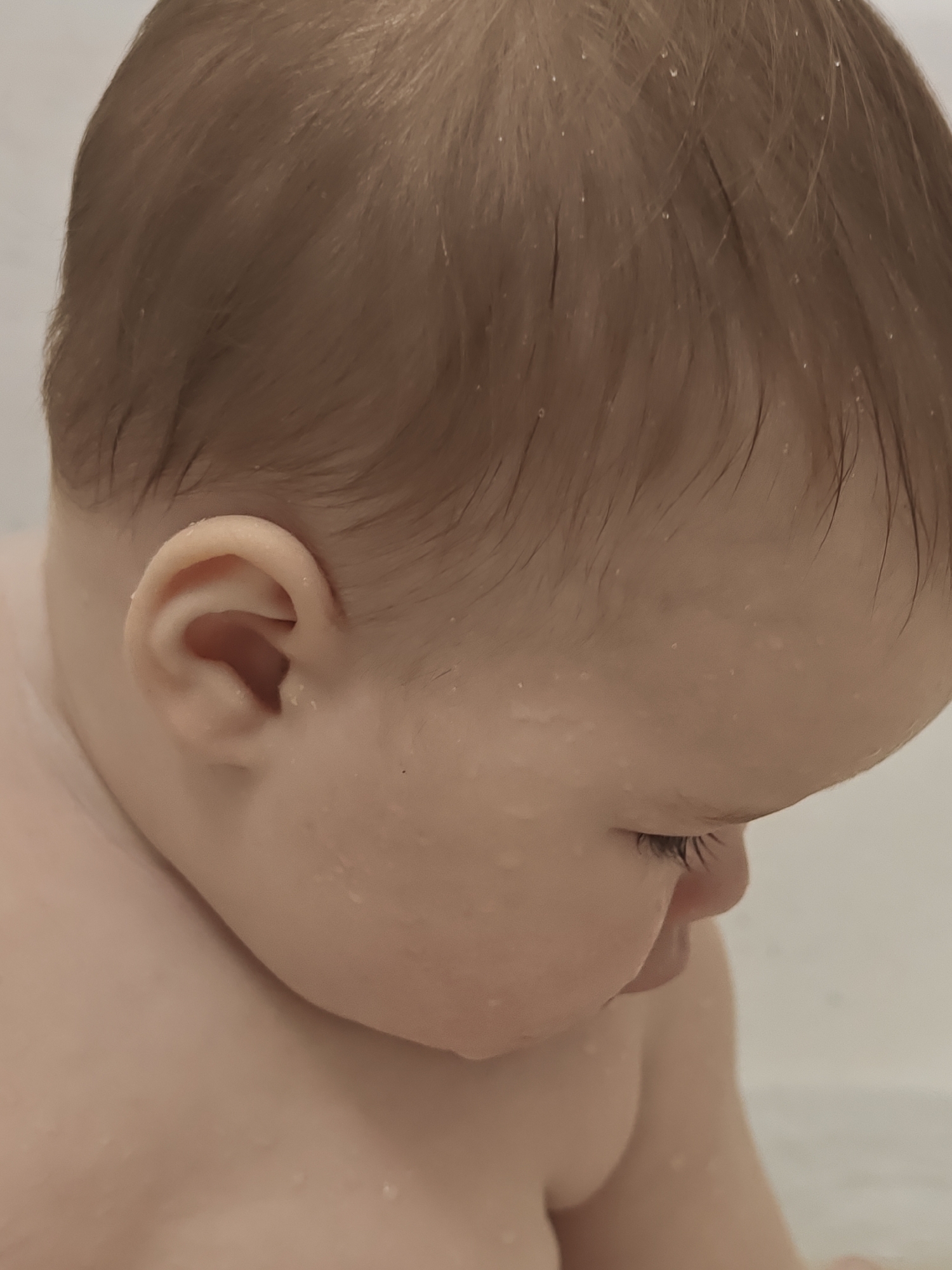 The image shows a close-up of a baby, likely during or after a bath. The baby has wet hair and water droplets are visible on their skin. The head is tilted downwards, and the eye is partially visible. The image does not provide any information about the location in Chaikovsky, Russia, or about any other details of the environment.