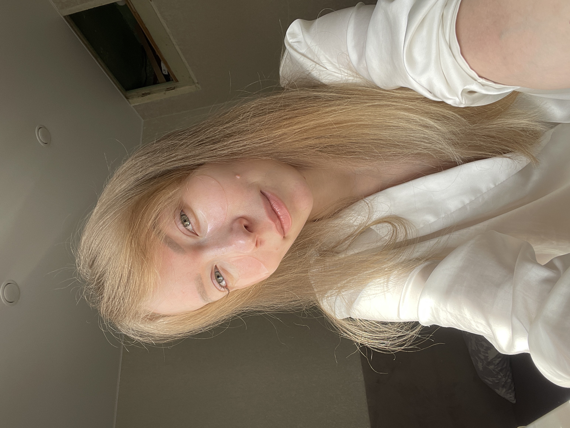 A fair-skinned individual with long blonde hair is photographed from a low angle. The person is wearing a white garment. The setting appears to be indoors, given the presence of a ceiling with an access panel. The location is not discernible as being Perm, Russia from the provided image.