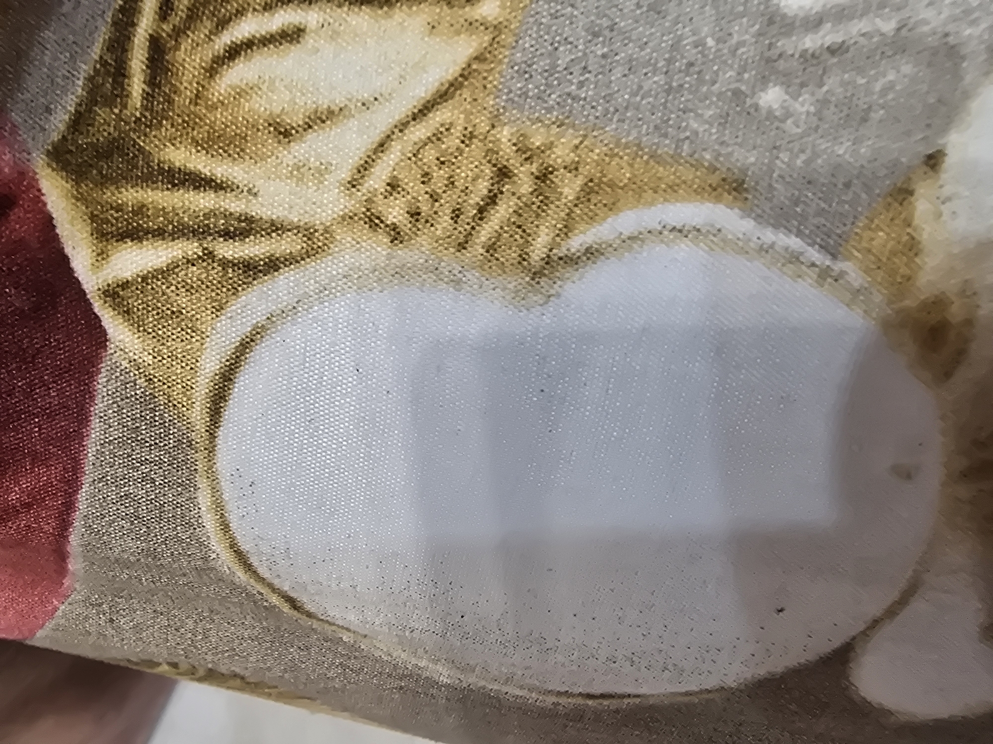 The image shows a close-up of a fabric with a pattern. The pattern appears to be abstract, with areas of white, gold, and a deep red or maroon color. There are also darker, possibly brown or black, lines or stripes in the gold section, suggesting a textured or striped design. The fabric has a visible weave. The lighting suggests it is indoors. There is no identifiable location in the city of Ulan-Ude, Russia, or any other specific geographical context. The image focuses solely on the textile.