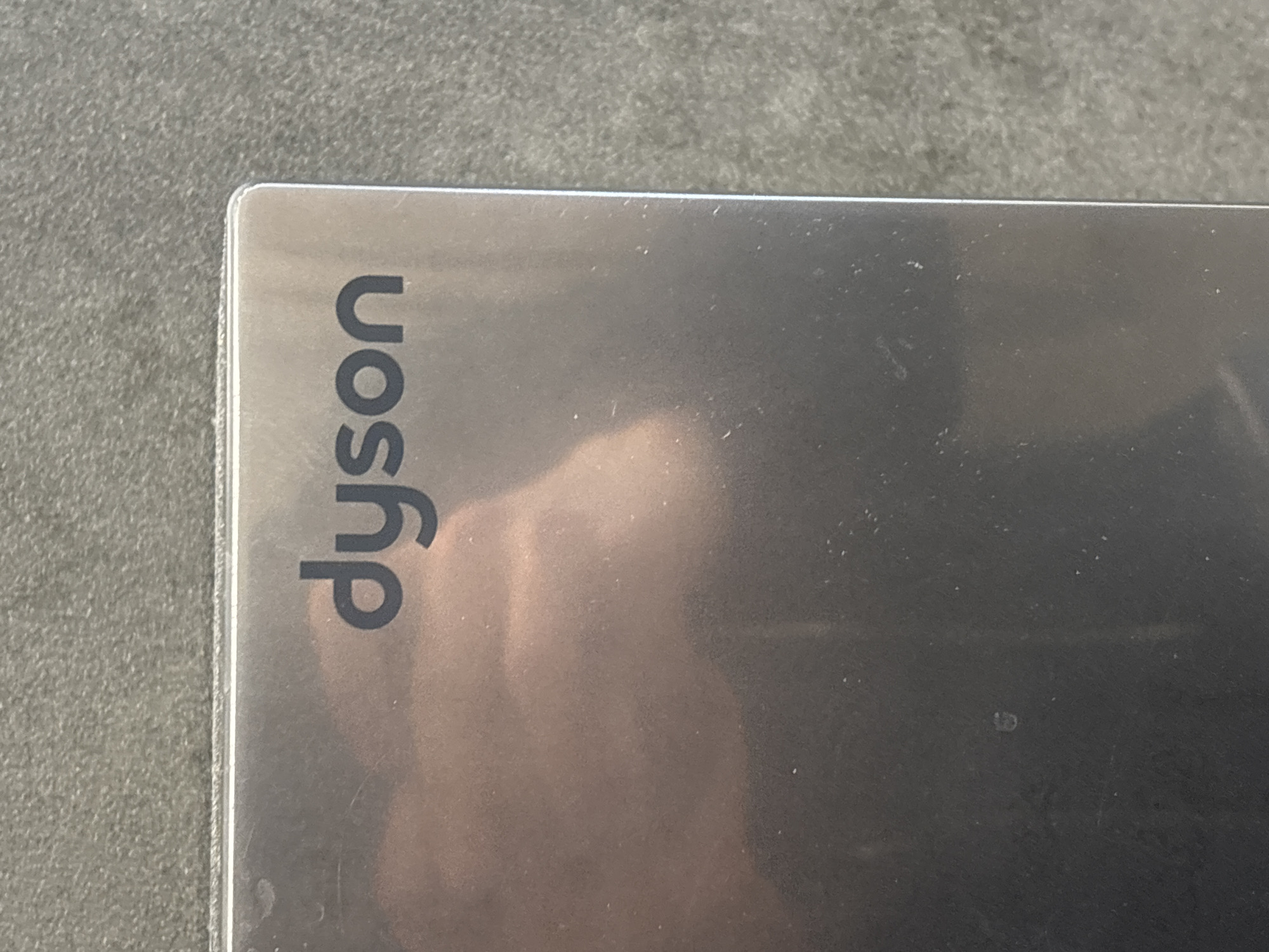 The image shows a corner of a silver-colored object with the word "dyson" printed vertically along the left edge. The background is a textured gray surface. The location is not apparent from the provided image.