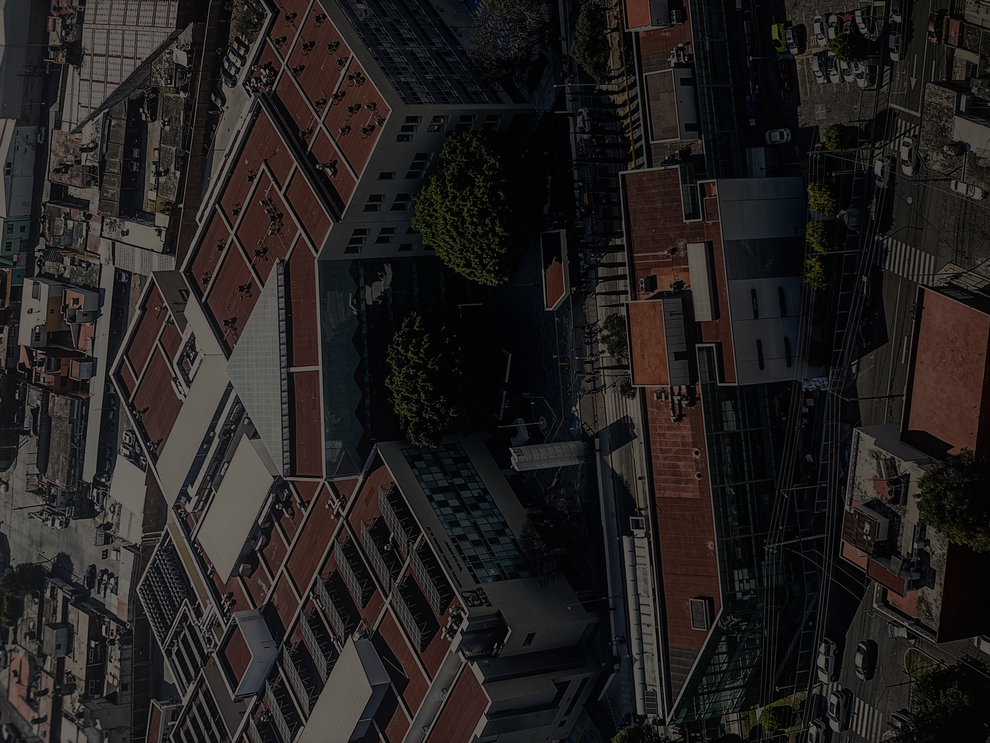The image is an aerial view of the Hospital General Regional No. 36, a public hospital operated by the Instituto Mexicano del Seguro Social (IMSS). The hospital is located in Puebla, Mexico. The image shows the rooftops of the hospital buildings, constructed with red tile roofs, courtyards with trees, and adjacent city streets and buildings. Cars are parked along the roads, and the area is surrounded by dense urban development.