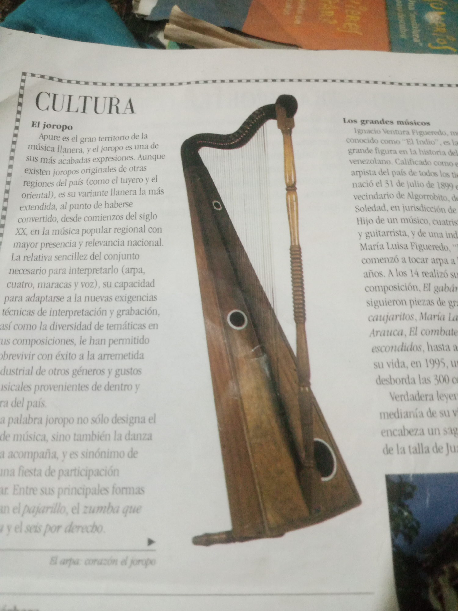 The image displays a page from a publication featuring an article about Venezuelan culture, specifically focusing on "El joropo" and "Los grandes músicos". A prominent visual element is a harp, a key instrument in joropo music, positioned centrally in the frame. The text discusses the origins and characteristics of joropo, mentioning Apure as its territory and its evolution in popular regional music. It also highlights Ignacio Ventura Figueredo, a renowned arpa player, and his contributions to Venezuelan music. The text does not specify a location in the city of Santa Ana, Venezuela. The image itself is a photograph of the printed page, with some background elements suggesting it's a part of a larger document or book.