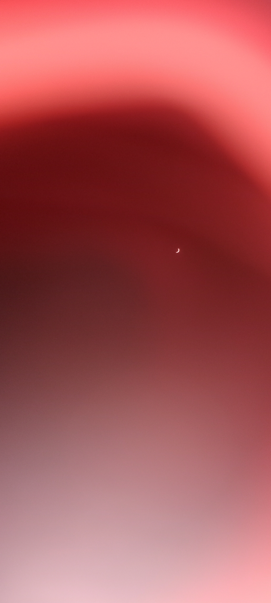 The image displays a gradient of red and pink hues, creating an abstract and atmospheric background. In the upper right quadrant, a small, crescent-shaped object, appearing as a thin white curve against the red, is visible. The overall impression is one of soft light and subtle color transitions, with the crescent object being the only discernible form.
