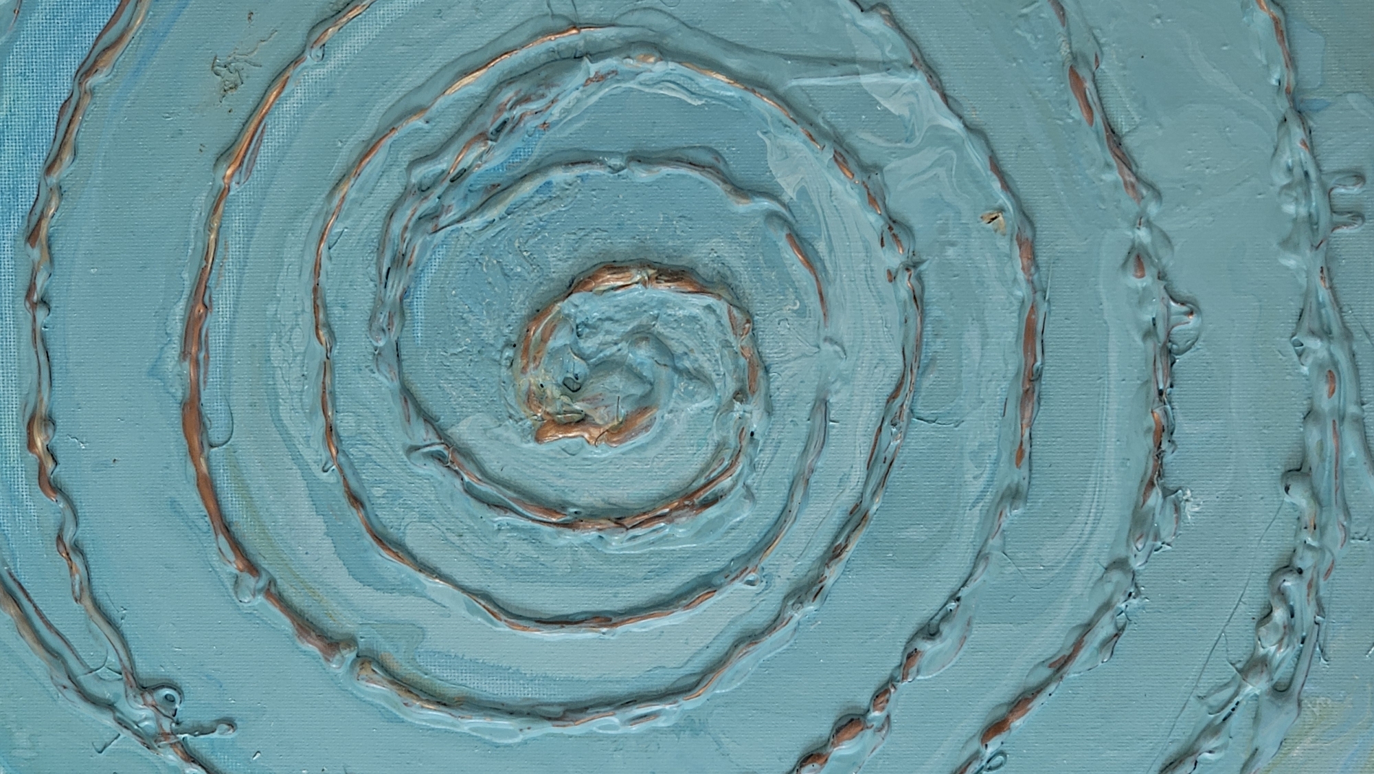 This is a close-up, abstract photograph of a painting. The painting features a blue background with a spiral design created using a textured medium, possibly paint or plaster. A metallic copper-colored line is embedded within the spiral, adding a contrasting element. The texture of the paint is thick and raised in places, with some drips visible. The overall impression is one of movement and depth. There are no discernible elements related to Baan Chaweng, Thailand, or any specific location within a city. The image solely focuses on the artistic details of the painting itself.
