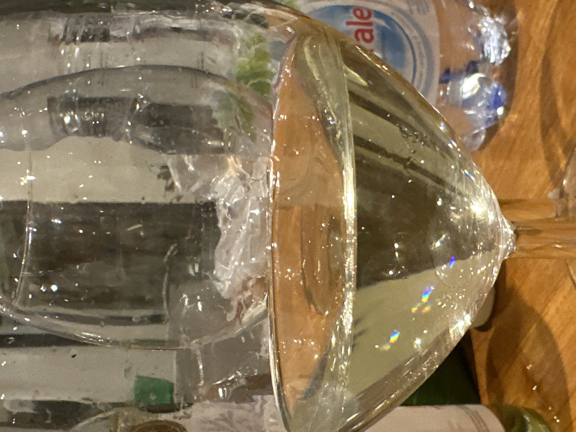 A close-up shot shows two water-filled wine glasses positioned on a wooden surface. A plastic water bottle is visible in the background, labeled with "ale". The scene is brightly lit, emphasizing the transparent nature of the glasses and the water within. It is impossible to confirm the location is Tumbak Bayuh, Indonesia based on the image. There is no mention of people.