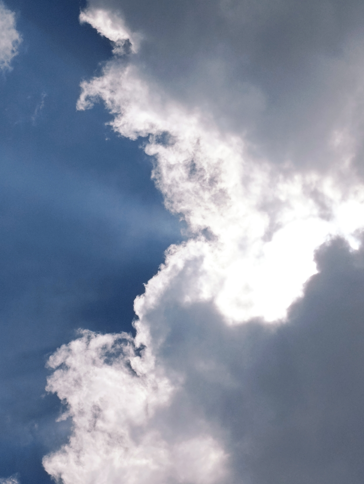 The image shows a dramatic sky with a mix of dark and light clouds. The sun is partially obscured by the clouds, creating a bright glow. The sky is predominantly blue, with shafts of light breaking through the clouds, suggesting a transition from stormy weather to clearer skies. There are no people, objects, or specific city elements visible, as the photograph solely captures the sky. The image does not provide any information about the city of Palchan, India, or any specific location within it.
