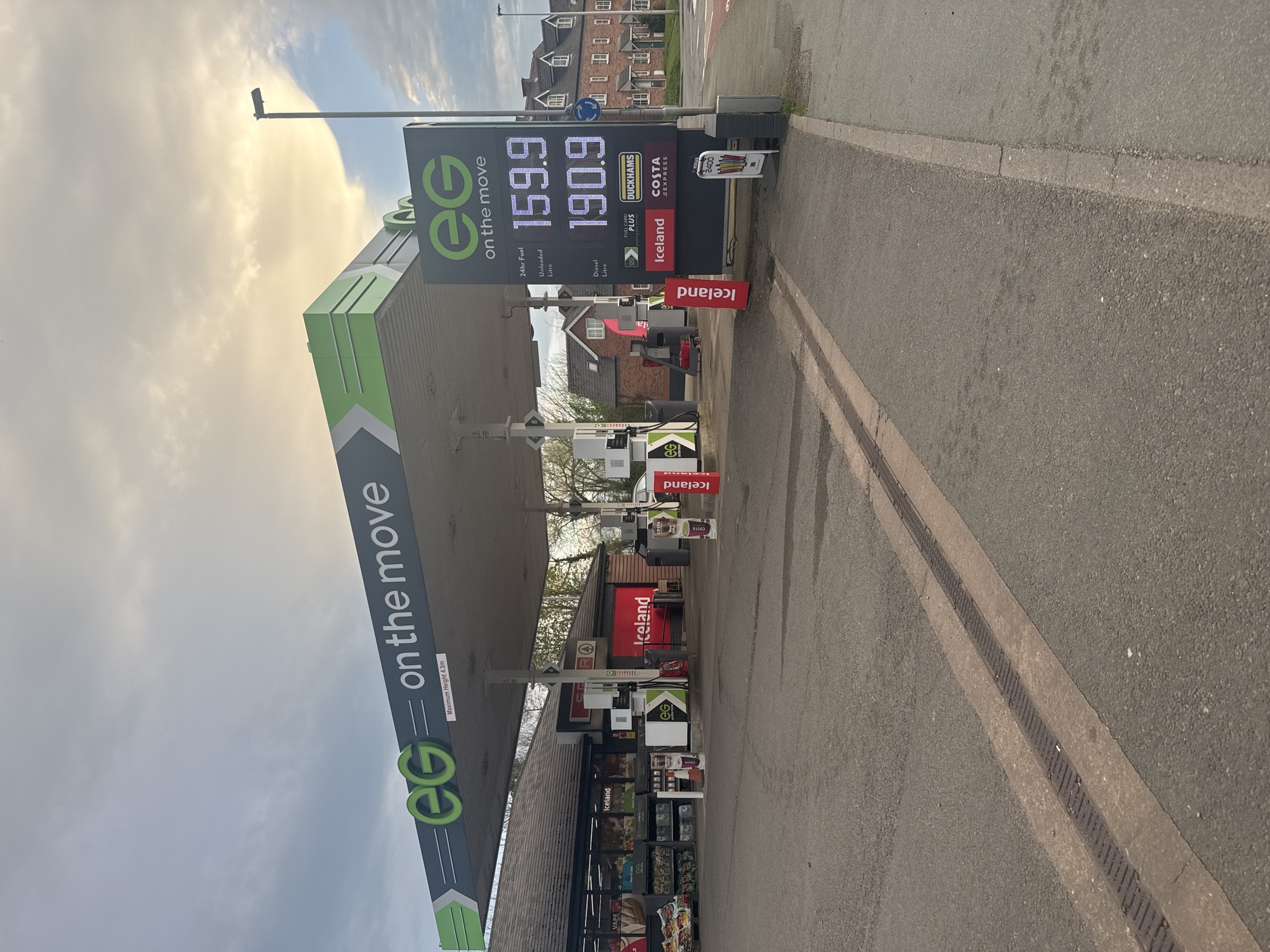 The image shows an EG "on the move" petrol station. The Unleaded fuel price is 159.9 per litre, and Diesel is 190.9 per litre. The station has an Iceland store, Duckhams fuel, and a Costa Express. The location is likely in Welshpool, United Kingdom. The photo appears to be taken from the roadside.