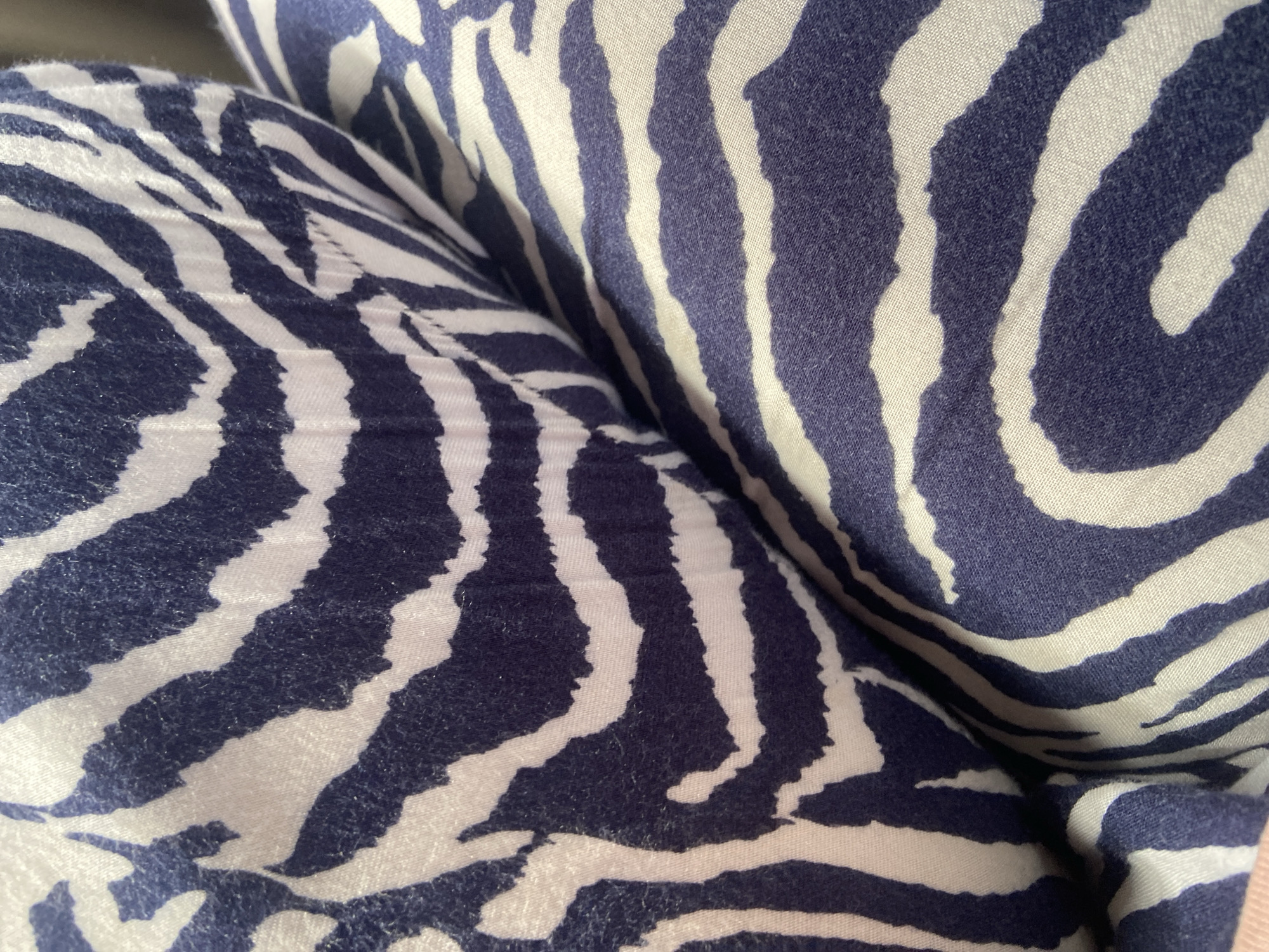 The image is a close-up, eye-level shot of a fabric with a navy blue and white zebra stripe pattern. The fabric appears to be soft and textured, possibly a pillow or cushion. The stripes are uneven and organic in shape, with some fuzziness visible on the edges, suggesting it might be a brushed cotton or a similar material. The lighting is soft and diffused, casting gentle shadows across the folds and curves of the fabric, highlighting its dimensionality. There are no people or other objects clearly visible in the frame, making the fabric the sole subject of the image. The setting is indeterminate; the image offers no clues about a specific location in Palopo, Indonesia, or any other city.