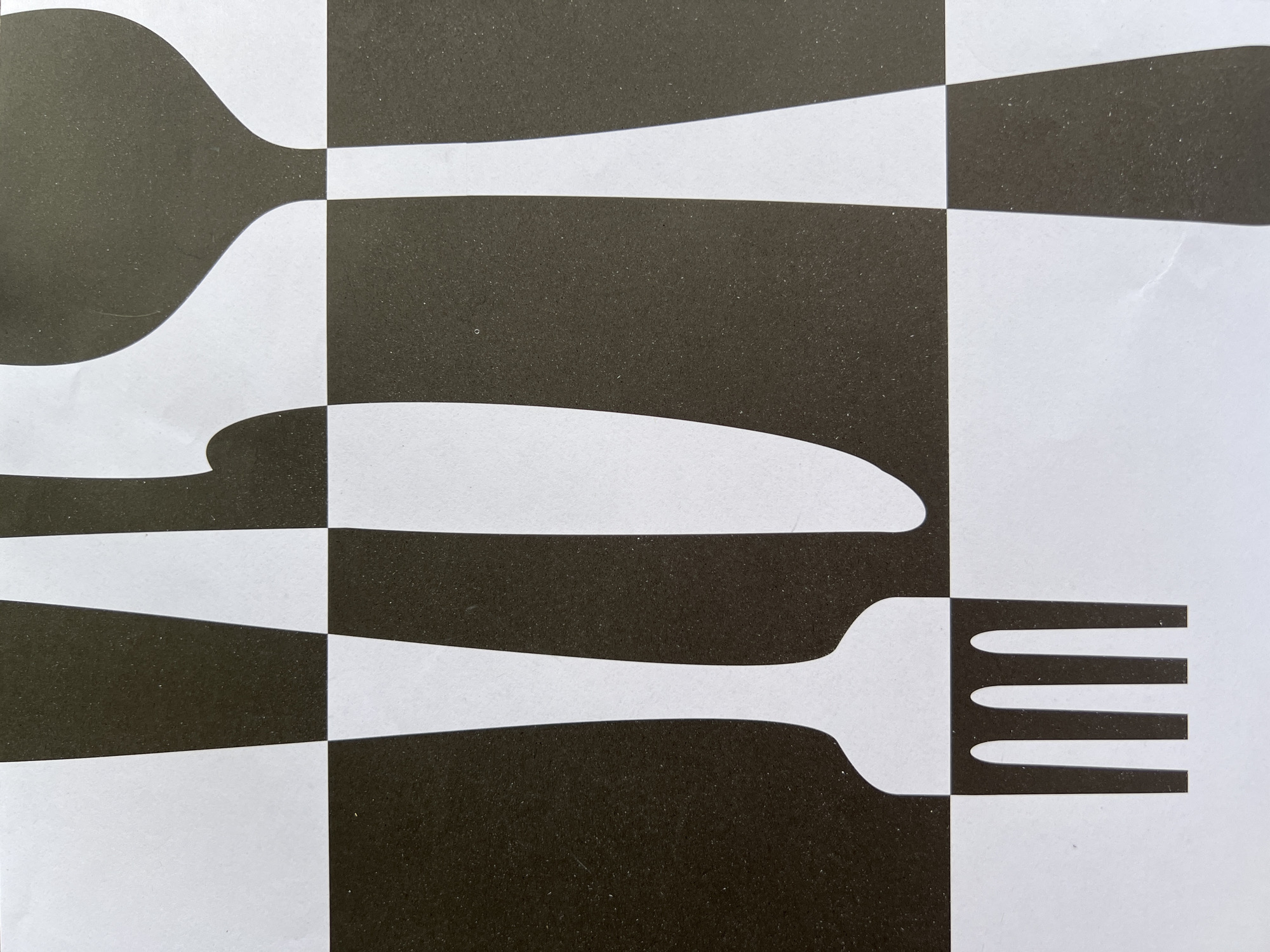 The image shows a close-up, abstract graphic design featuring bold black and white shapes. The design appears to be a stylized representation of cutlery, with elements resembling a fork, knife, and spoon. The shapes are geometric and sharp, creating a strong contrast. The background is a grid-like pattern of alternating black and white squares, which further enhances the abstract and graphic nature of the artwork. There are no people, animals, or natural elements visible in the image. The image does not provide any information about its location in the city of Eretria Municipal Unit, Greece.