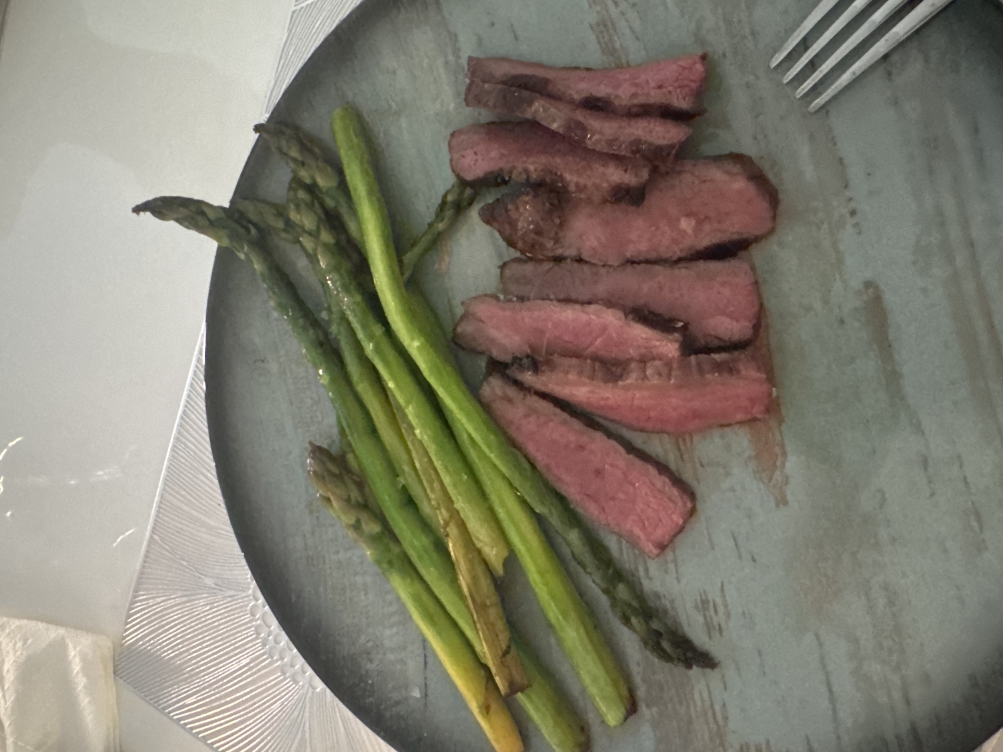 A plate of sliced steak and asparagus is shown on a plate. A fork is located on the upper right side of the plate. The plate is on a table with a decorative surface. The image does not provide information about the location in Sofia, Bulgaria, or the presence of people, actions, interactions, or additional environmental details.