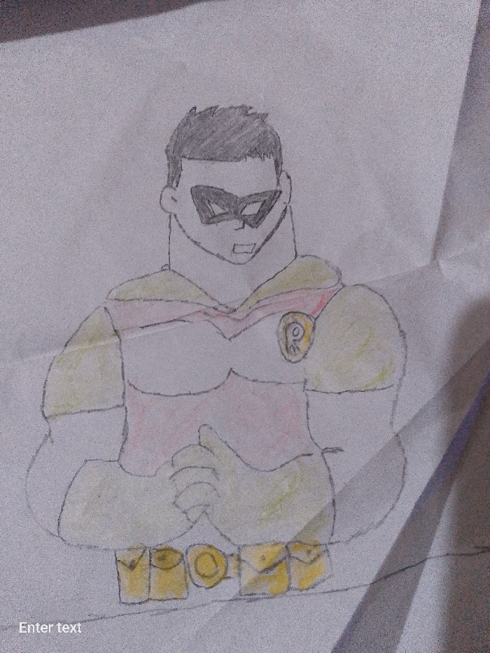 A hand-drawn image depicts a superhero-like figure on a white, possibly crumpled piece of paper. The figure is wearing a mask over his eyes, and his hair is short and dark. He is depicted with a muscular build, wearing a costume with red, yellow, and white elements. A stylized "R" is visible on his upper arm. The figure's hands are clasped in front of him. A belt with pouches is visible around his waist. The location is unknown.