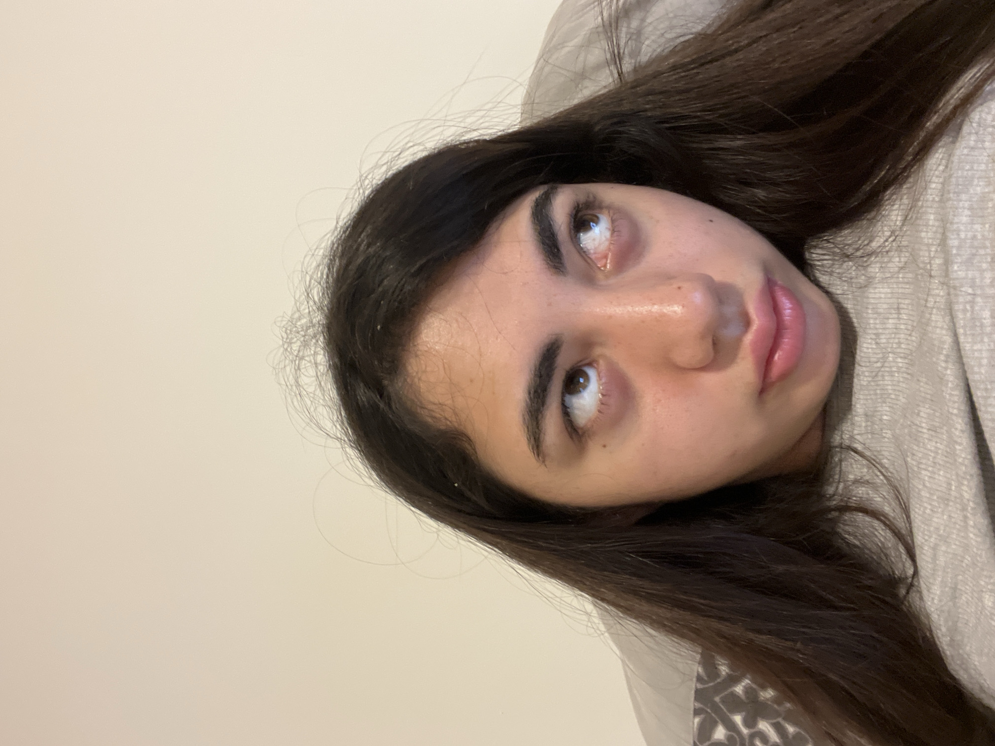 A young woman with dark hair is looking up and to her right. She is wearing a grey sweater. The background is a plain, beige wall. The image is a close-up of her face and upper body. The location is not identifiable from the image itself, and therefore any mention of Chotěšov, Czechia would be speculative.