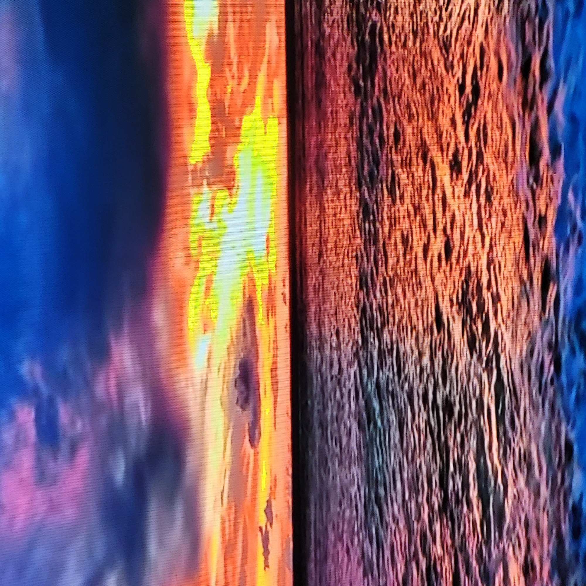 The image is a close-up shot displaying an abstract, textured composition divided into distinct sections. The left side shows a dark blue and pink clouded effect, transitioning to a brighter yellow and orange area resembling a flame or light source. The right side presents a dense pattern of raised, irregular lines, colored in shades of orange, brown, and blue, suggesting a rough, uneven surface. There are no people or discernible objects present in the image beyond the abstract patterns. The environment appears to be an abstract display. The location in Yerevan, Armenia is unknown.