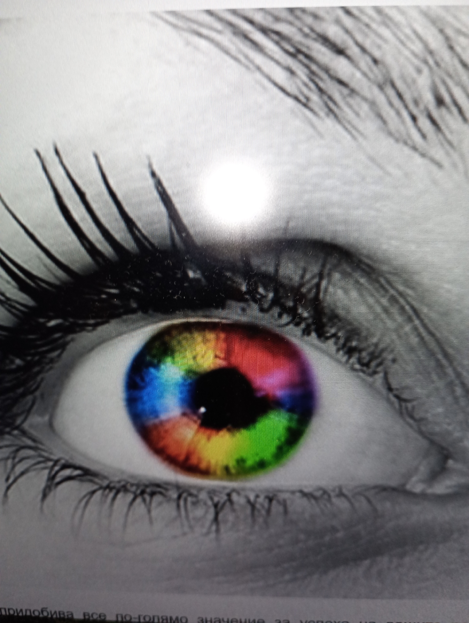 The image shows an extreme close-up of a human eye with a rainbow-colored iris. The eyelashes and eyebrows are dark and prominent. The surrounding skin is desaturated, creating a stark contrast with the vibrant colors of the iris. There are no discernible elements that indicate a specific location in Harmanli, Bulgaria, or any other city. The image appears to be a digitally enhanced photograph or artwork of an eye.