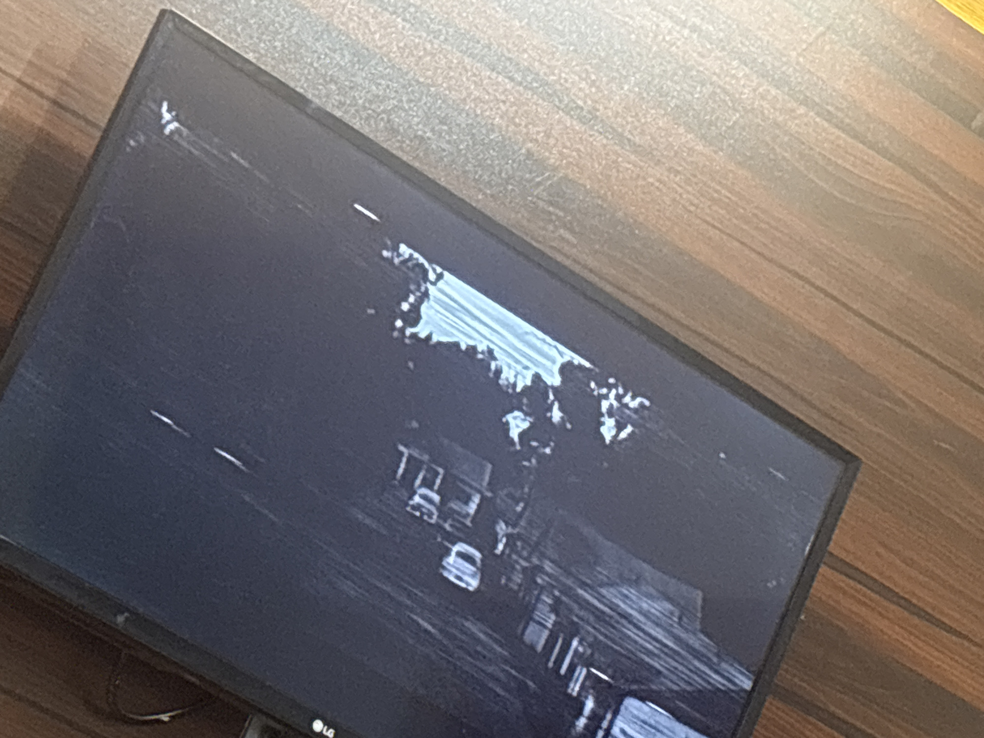 A television, an LG brand, sits on a wooden surface. The screen displays an image from a camera located on a street in Eneka, Nigeria. Multiple cars are on the street. Houses are visible along the street.