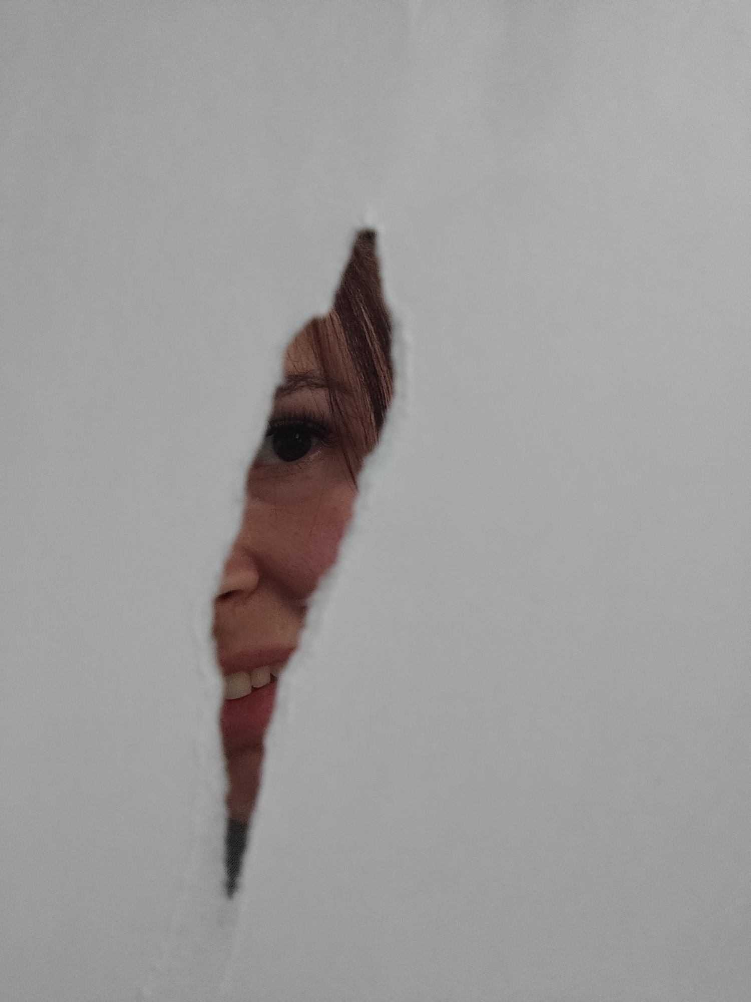 A partial view of a person's face is visible through a torn piece of white paper. The visible portion of the face includes an eye, nose, mouth with teeth, and part of the hair. The background is indistinct. There is no evidence to connect this image to Фоки, Russia.