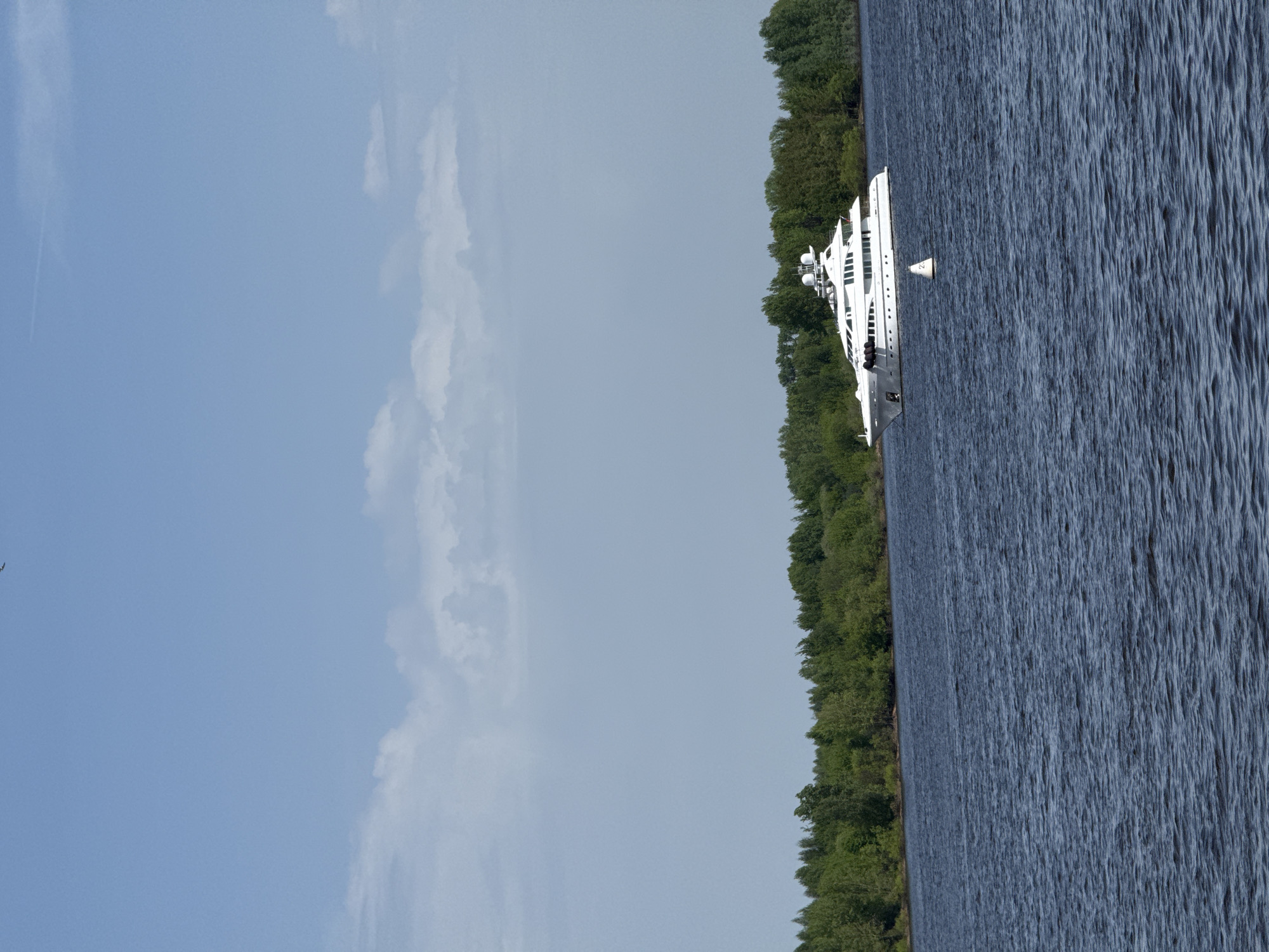 The image shows a yacht on the Volga River in Nizhny Novgorod, Russia. The yacht is white and has multiple decks. It is located near a shoreline with trees. The water is rippled, and the sky is light blue with some clouds.