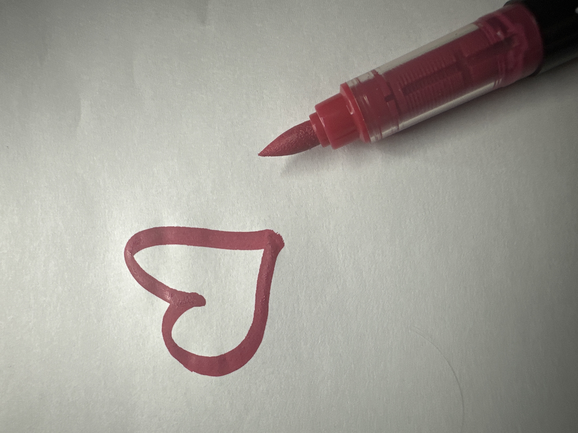 A red marker lies on a white sheet of paper. Next to the marker is a red heart drawn on the paper. The location is not identifiable.