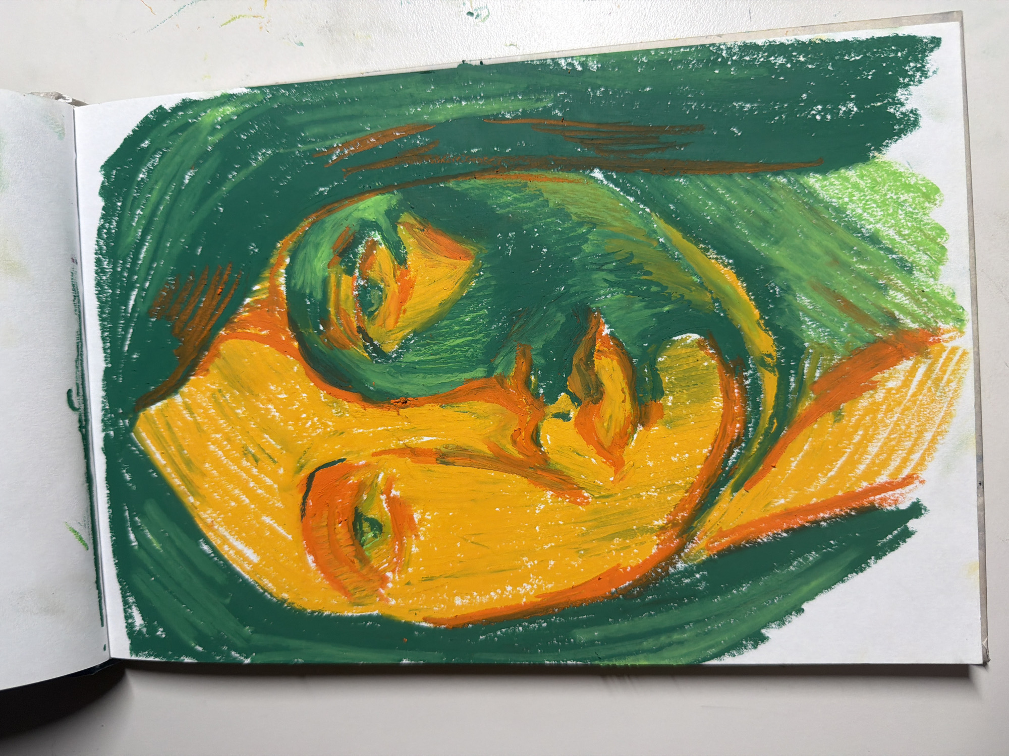 The image shows a close-up, overhead view of a drawing of a face rendered in oil pastel on white paper within a sketchbook. The drawing features a face with prominent features, depicted with bold strokes of yellow, orange, and green. The left side of the face and hair are primarily yellow and orange, while the right side and hair are predominantly green, creating a strong contrast and suggesting a play of light and shadow. The eyes are detailed with green and orange, and the lips are rendered in orange. The background is filled with green strokes, extending beyond the face to frame it. The sketchbook is open, revealing the textured paper and the medium used. The background outside the sketchbook is a plain, light-colored surface. There is no discernible location in Dongducheon-si, South Korea, evident in the image; it is a depiction of a piece of artwork.