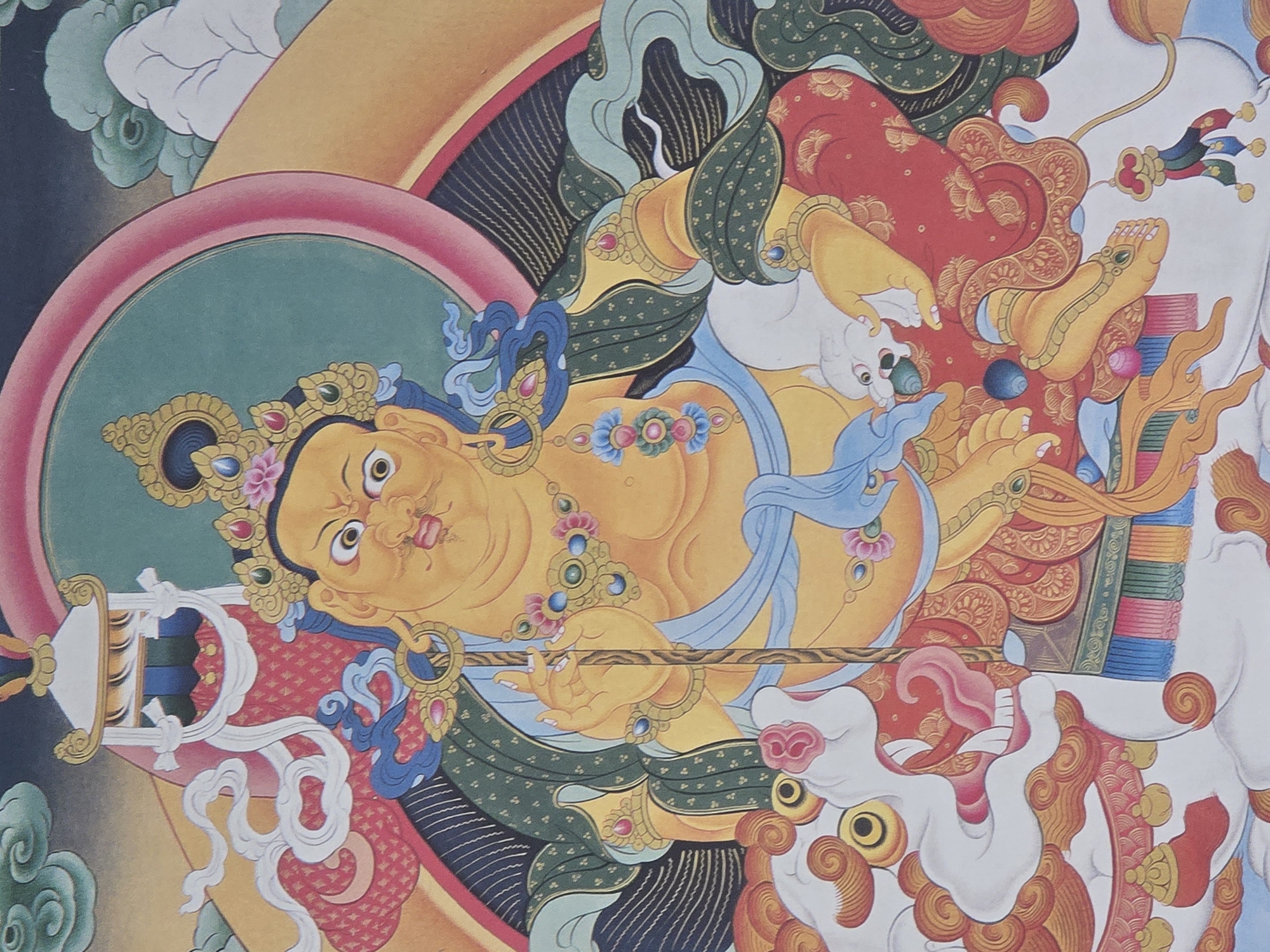 This is a close-up, eye-level, vertical shot of a Tibetan thangka painting depicting a multi-limbed deity, likely a wrathful deity from Buddhist iconography, seated on a white lion. The deity is yellow-skinned, with a large, round face, bulging eyes, and a stern expression. They wear an elaborate crown adorned with jewels and a pink flower, and several necklaces of beads and pendants. The deity's body is plump and adorned with gold jewelry. The left hand rests on a staff, while the right hand is held in a gesture of offering or protection.
The deity is clad in green robes with a dark patterned lining and red trousers. The lion is depicted with a fierce expression, open mouth, and flowing mane, its body white with red and gold ornamental details. The background features swirling clouds in muted tones of green, yellow, and blue, with a large circular halo of pink and teal behind the deity.
The style is characteristic of Tibetan thangka paintings, with bold outlines, vibrant colors, and intricate details. The painting appears to be in good condition, with no visible damage. This artwork is not located in the city of Ulan-Ude, Russia.