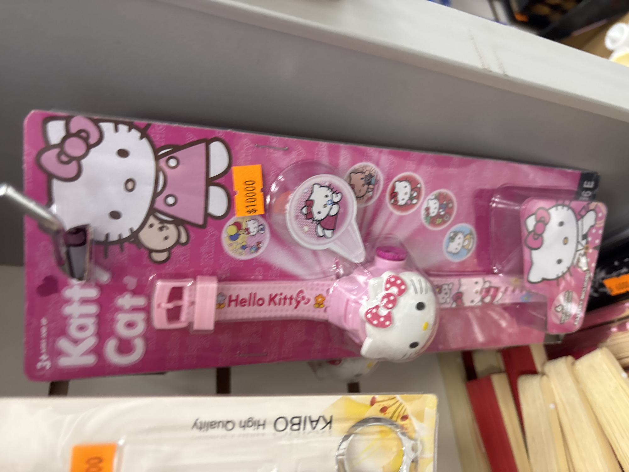 The image shows a Hello Kitty watch set on a store shelf. The set includes a watch and a magnifying glass, both decorated with Hello Kitty designs. The packaging is pink with Hello Kitty characters and patterns. A price tag on the package reads "$10000". Other items are visible on the shelf below the watch set. The location is potentially a retail store in Buenos Aires, Argentina.