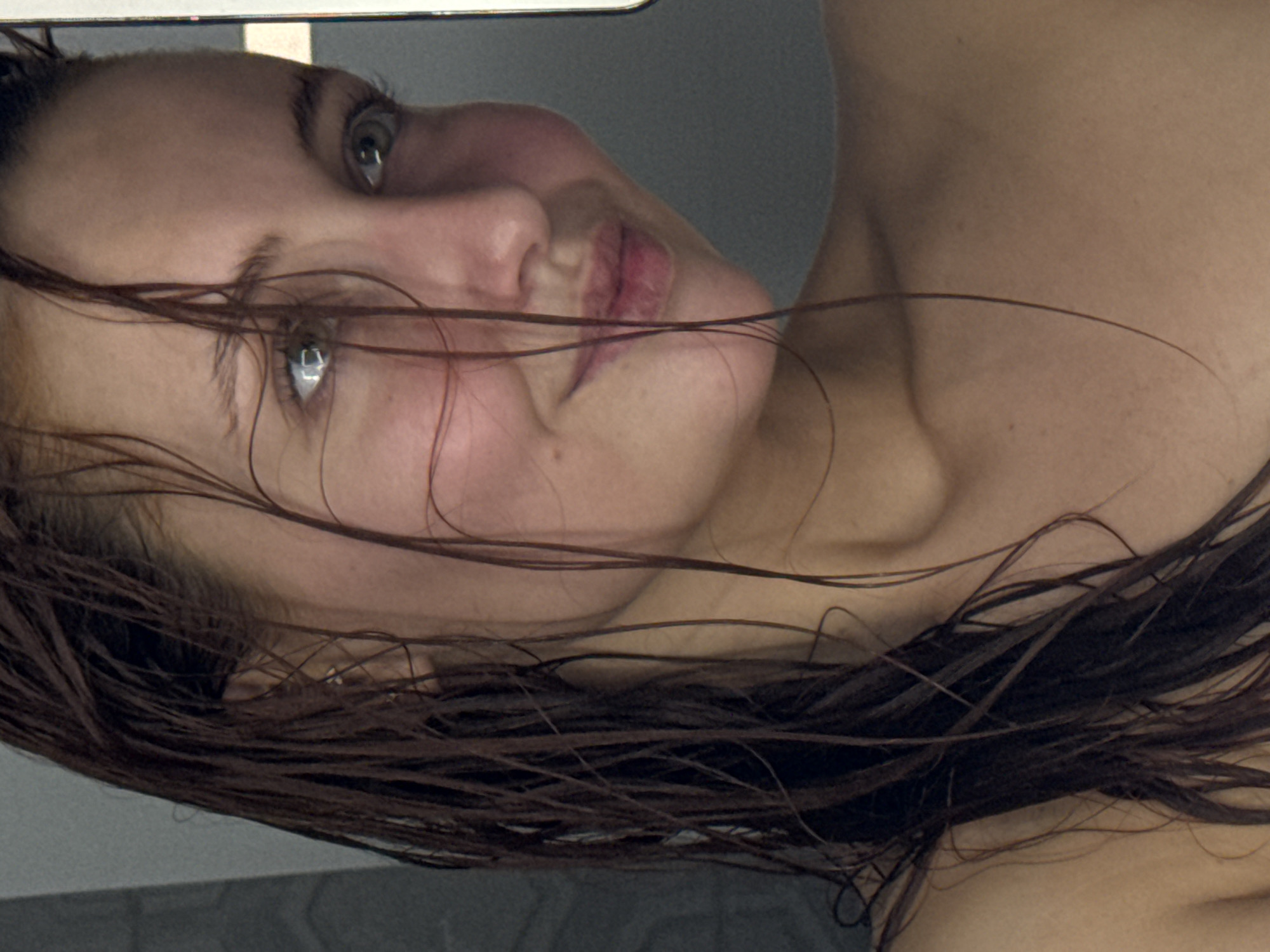 The image shows a woman with wet, brown hair lying down. Her face is visible, and she appears to be looking upwards. The background is a blurry gray. The setting cannot be determined without additional information. There is no indication that this image was taken in Chaikovsky, Russia.