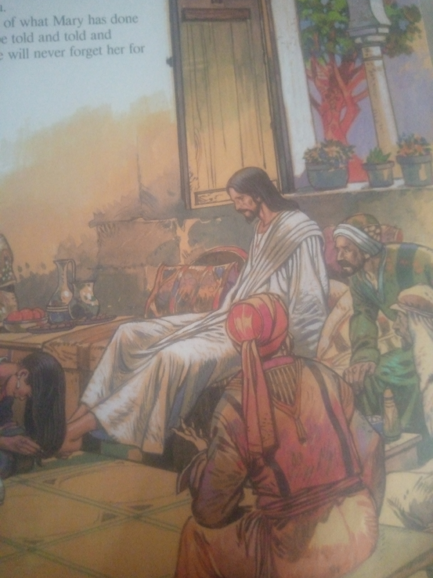 The image depicts a scene from a religious painting, possibly illustrating a biblical narrative. In the foreground, a person with long dark hair is kneeling, tending to the feet of a man seated on a low couch. This seated figure is Jesus, identifiable by his traditional depiction with a beard and wearing a white robe with stripes. He is in the center of the image, reclining on a divan adorned with patterned cushions. To his right, another man, wearing a green tunic and a turban, is observing the scene. Behind them, an architectural setting is visible, with wooden doors and an open area revealing potted plants and a tree against a pale wall. The overall impression is one of reverence and an intimate moment. The text on the left side of the image appears to be part of a narrative that accompanies the illustration, possibly detailing the actions of "Mary." The prompt's mention of Jauro Yinu, Nigeria, is not visually supported by the image itself, which depicts a scene consistent with ancient Judea or a similar historical context.