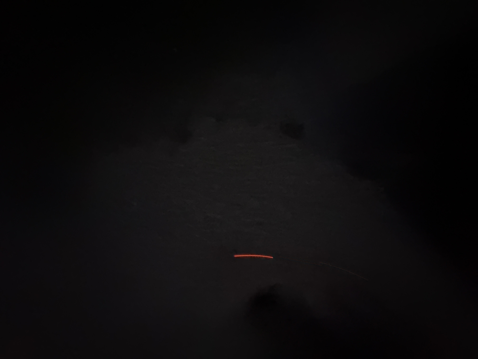 In a dark environment, a thin, bright orange line appears vertically in the center-left of the image. The line is approximately two inches long. Faint shadows or textures are discernible in the background.