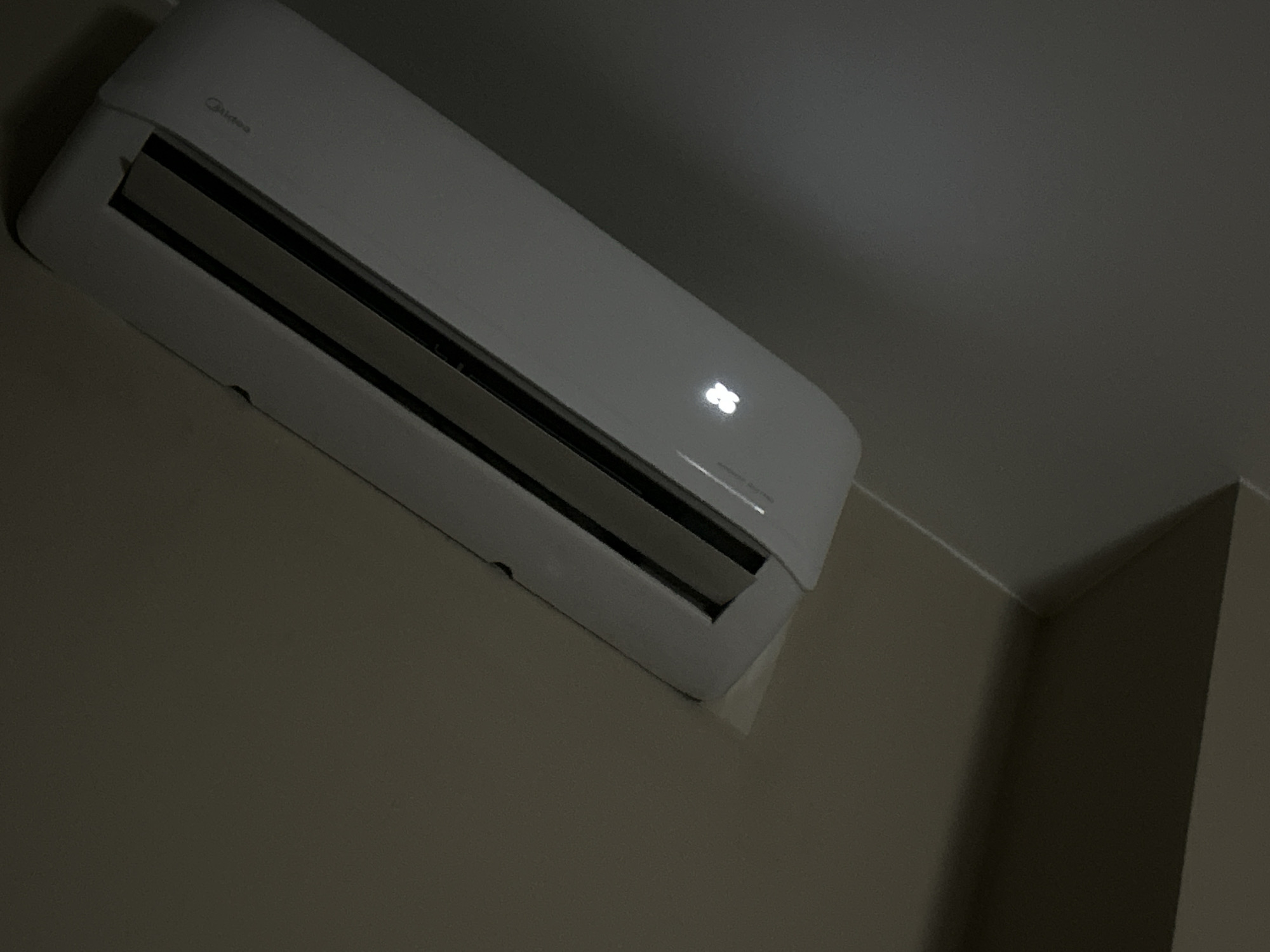 The image shows a Midea brand air conditioner mounted on a wall. The wall and ceiling are painted in neutral tones. The air conditioner's display shows the number "26." The scene is indoors. No people are visible. There are no indications of the location being Plovdiv, Bulgaria.
