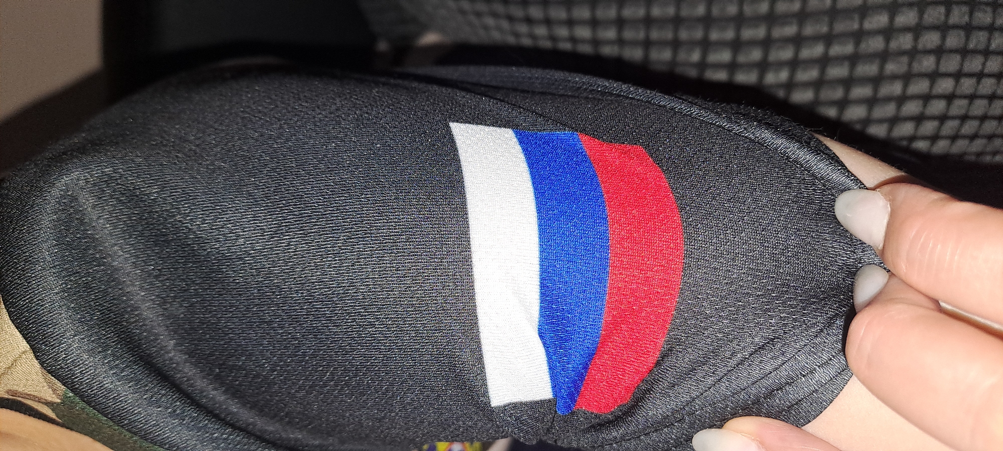 A close-up photograph shows a black fabric item with a vertical tricolor stripe of white, blue, and red, resembling the Russian flag. A hand is visible near the edge of the fabric. The environment is dark and undefined. There is no information to suggest that the image was taken in Yekaterinburg.